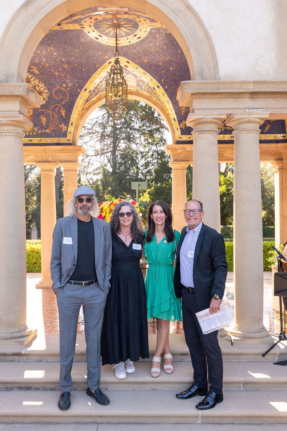 Four people smiling together under an ornate archway with columns at an outdoor event venue.