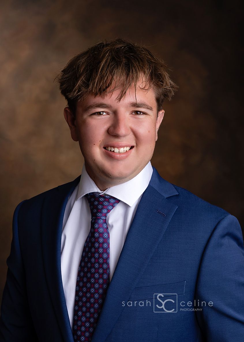 Young man in blue suit and patterned tie smiling in a professional portrait photo by Sarah Celine Photography.