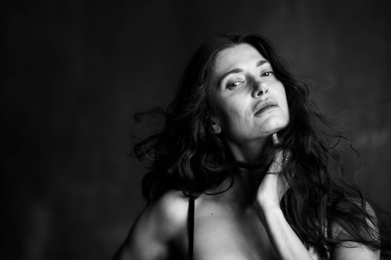 Black and white close-up portrait of a dark-haired woman gazing upward with hand on neck.
