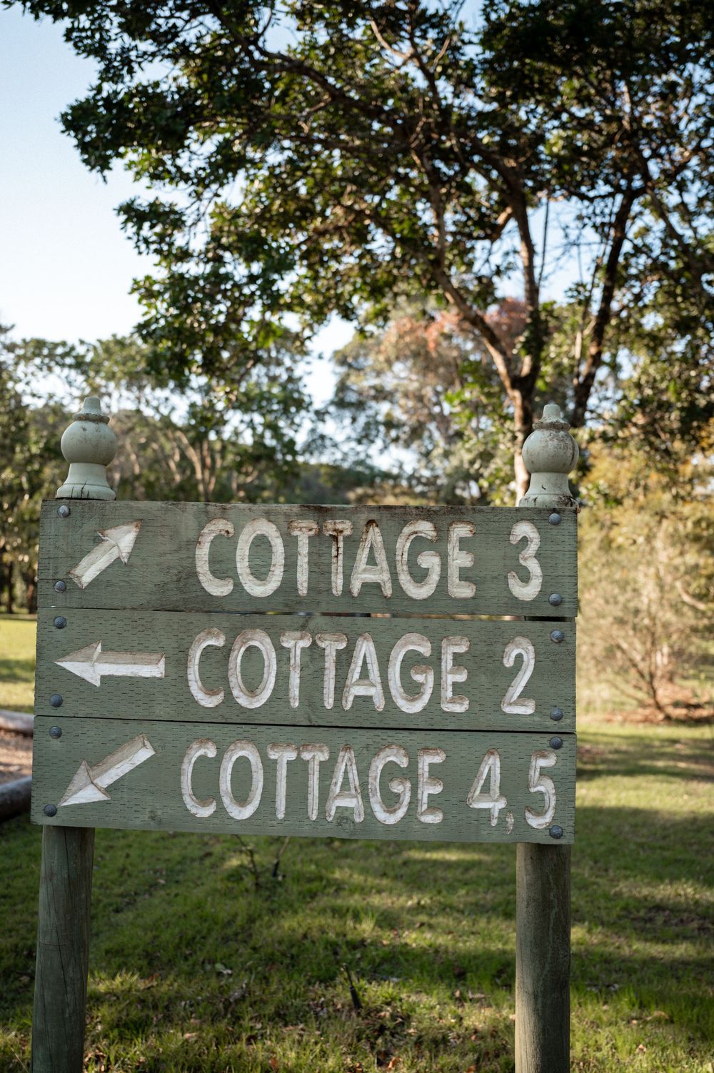 Rustic wooden directional sign pointing to Cottage 2, 3, and 4.5 surrounded by lush green trees.