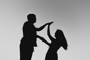 Black and white silhouette of two people in a dramatic confrontation against a gray sky background.