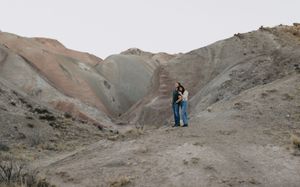 Two people embracing on a desert trail surrounded by colorful eroded badlands hills.