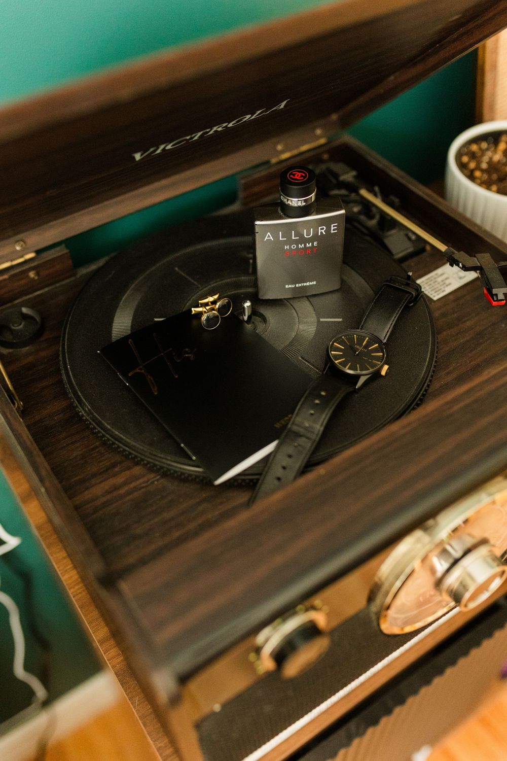 Victrola record player styled with Allure Homme cologne, a black watch, and cufflinks on a vinyl record.