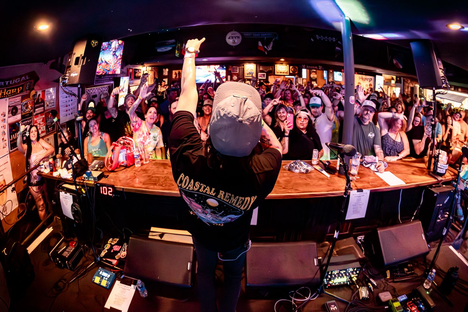 Musician singer performs for cheering crowd at a lively bar, fish-eye lens captures energetic nightlife scene.
