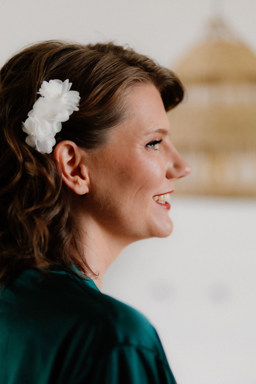 Smiling woman in profile view wearing a green satin robe and white floral hair accessory.