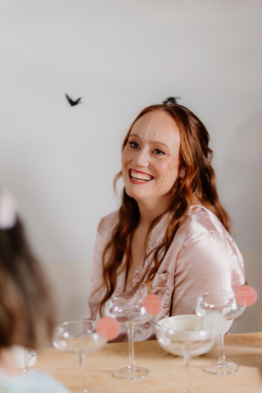 Smiling redhead woman in pink satin blouse sitting at table with champagne glasses at a celebration.