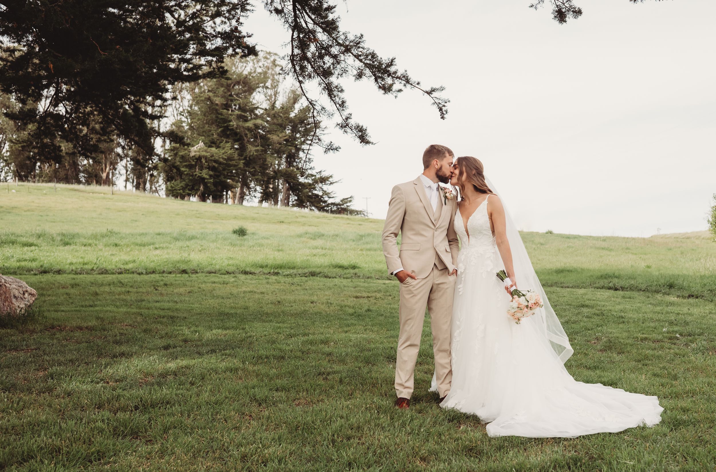 Bride and groom share a romantic moment on lush green lawn surrounded by trees in outdoor wedding photo.