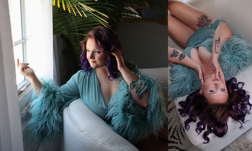 Woman in teal fur robe with purple hair poses by window and reclines on white sofa in boudoir photo session.