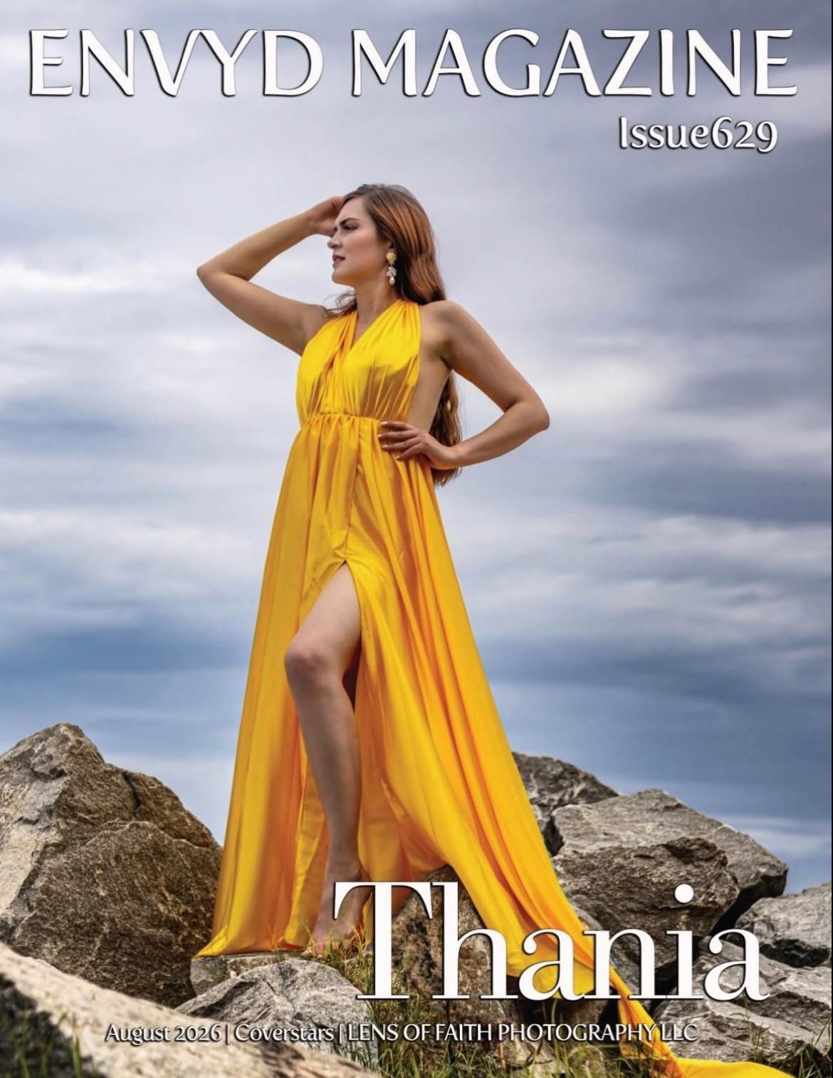 This magazine cover from ENVYD Magazine features a model in a flowing yellow gown posing on rocky terrain under a cloudy sky.