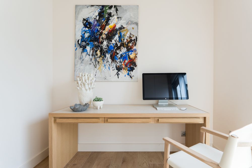 Modern home office with wooden desk, iMac computer, and colorful abstract wall art in a bright white room.