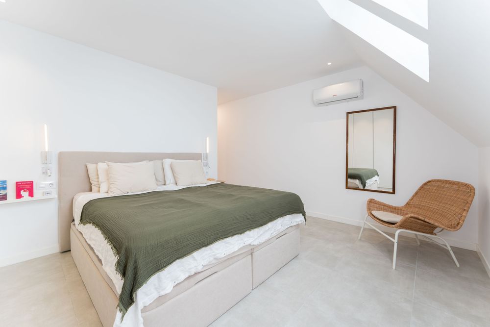 Bright minimalist bedroom with green bedspread, rattan chair, skylight, and white walls in a modern home.