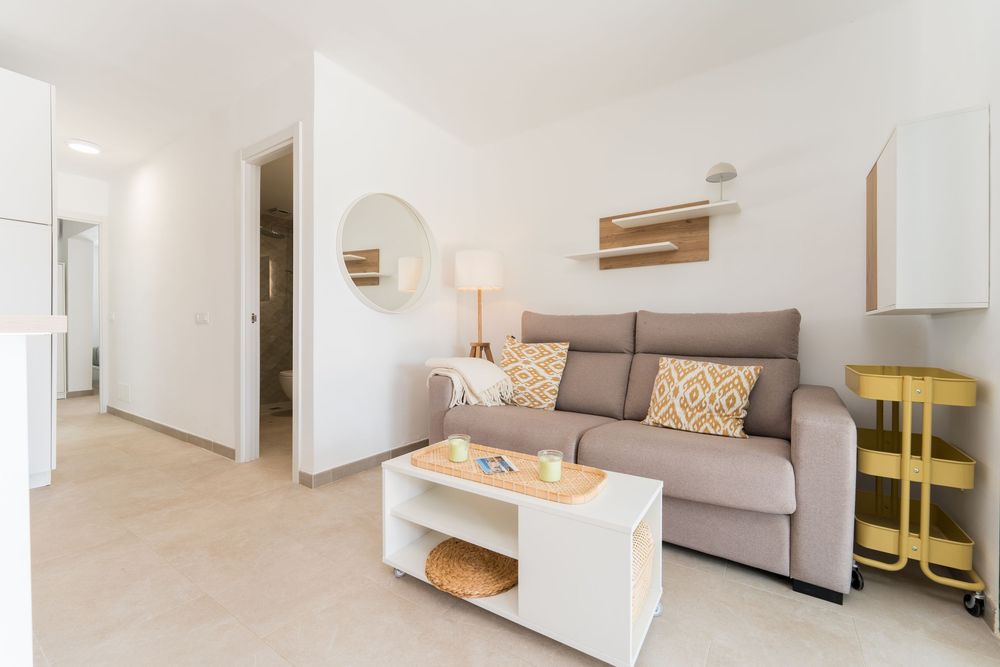 Modern bright living room with gray sofa, yellow accent pillows, white coffee table, and minimalist decor on light tile floors.