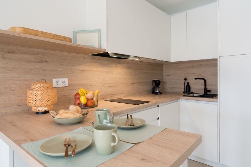 Modern white kitchen with wood countertops, induction cooktop, coffee maker, and a table set with mugs and fresh fruit.