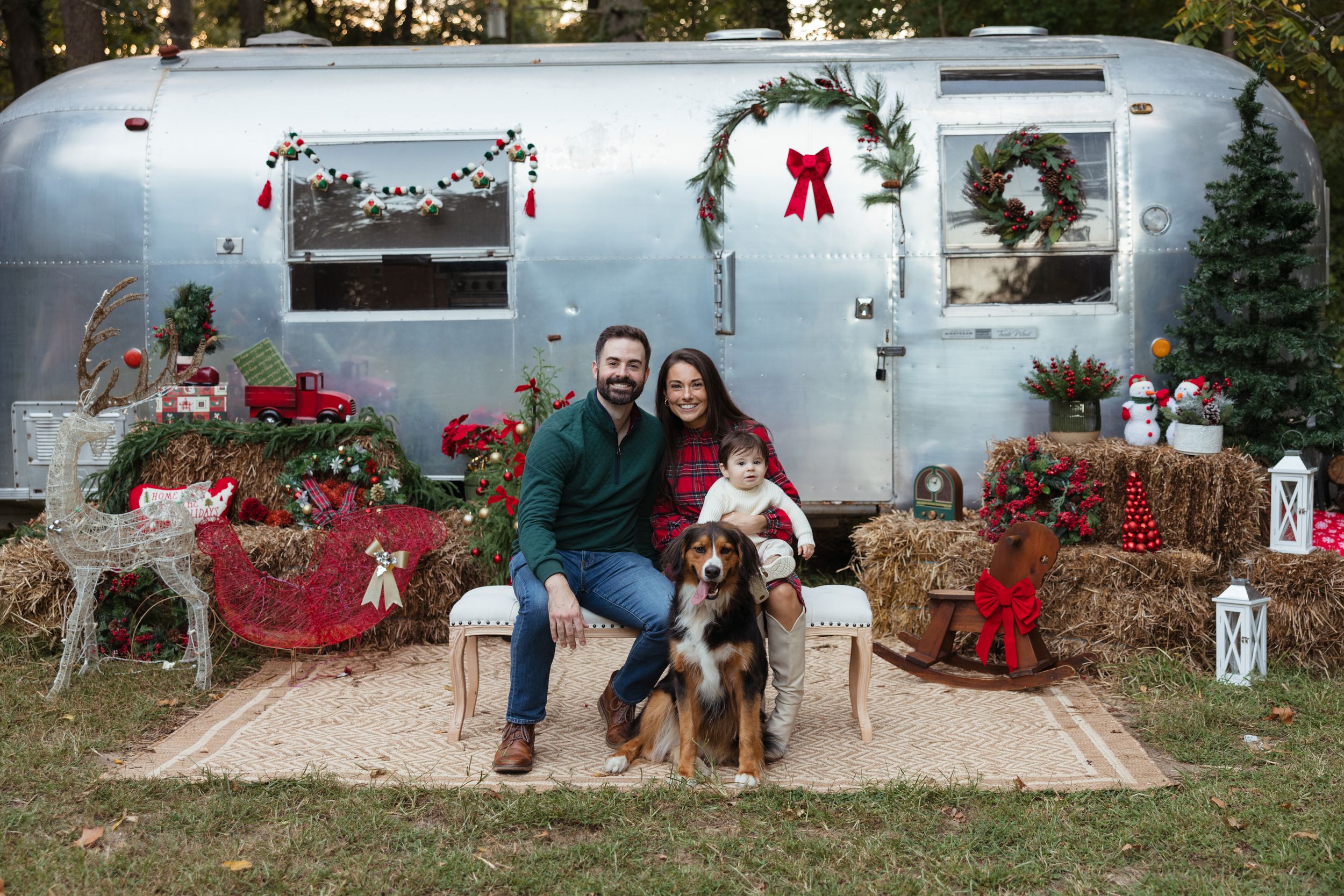 Family with dog poses for Christmas photo by decorated vintage Airstream trailer for a Holiday mini session at Root and Rise in Medford, NJ.