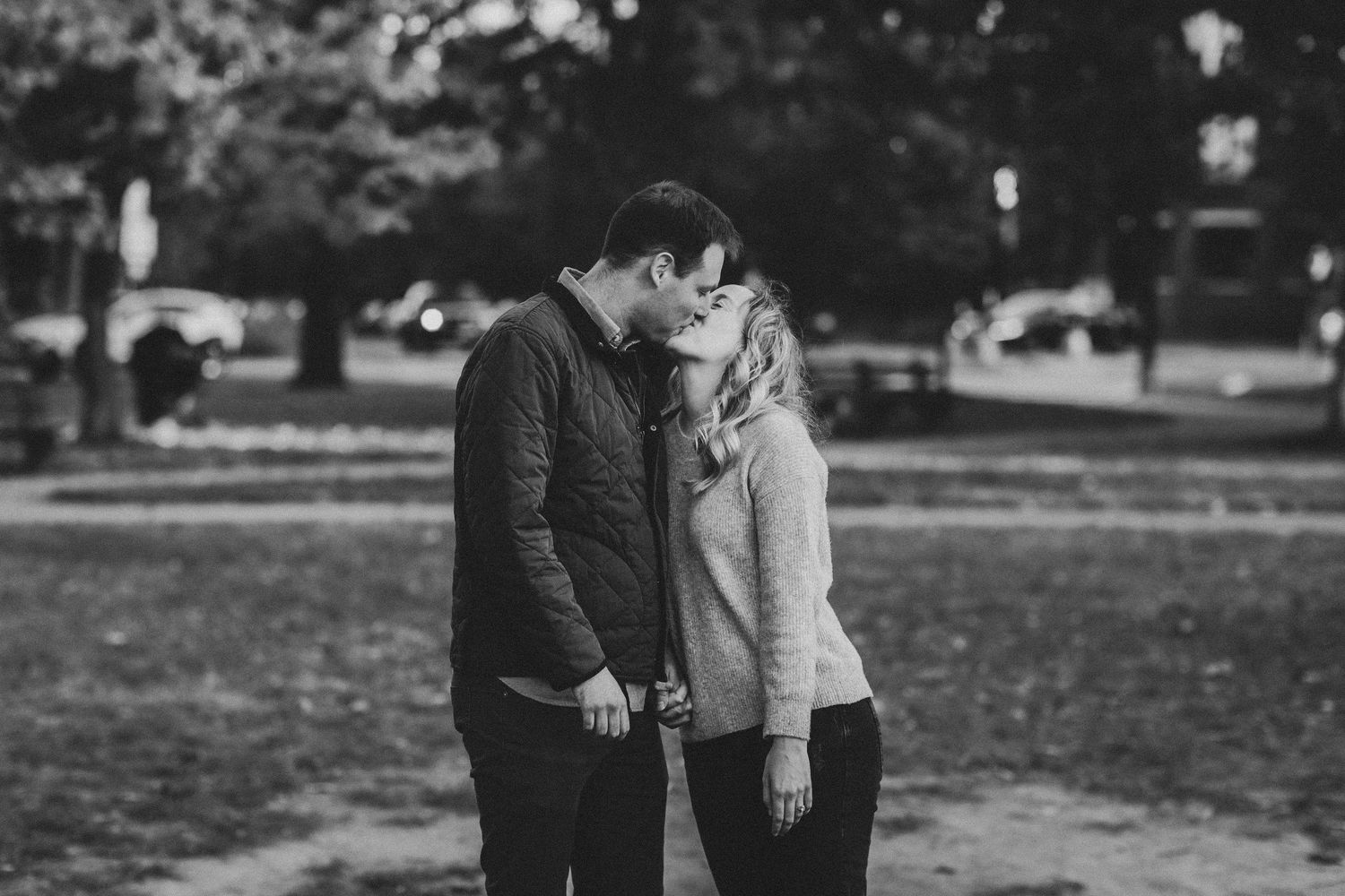 Black and white photo of a couple sharing a romantic kiss in a park, holding hands outdoors at the Stanton Park in washington DC