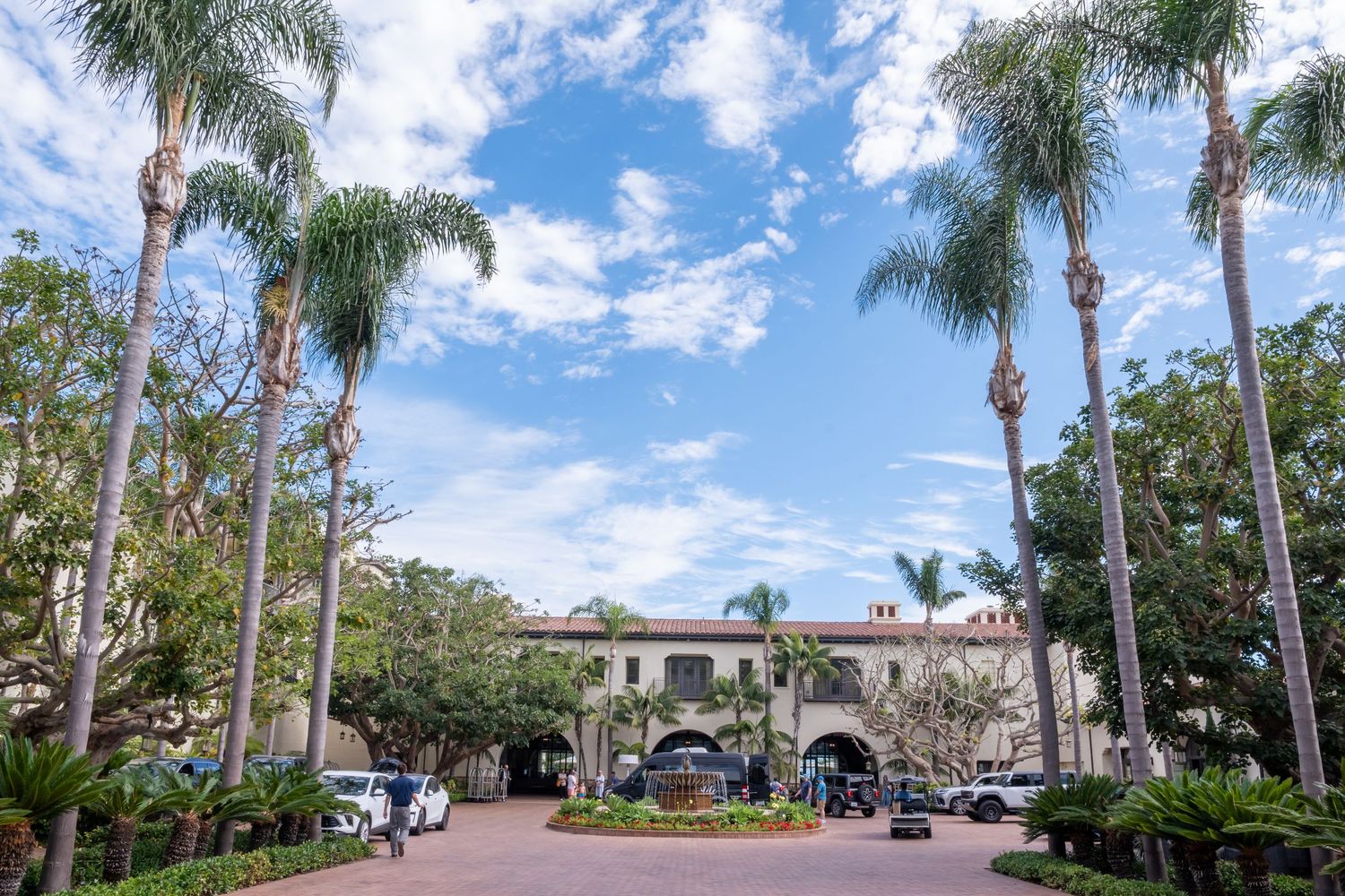 Grand Spanish Colonial building entrance with tall palm trees under blue skies in sunny Southern California.