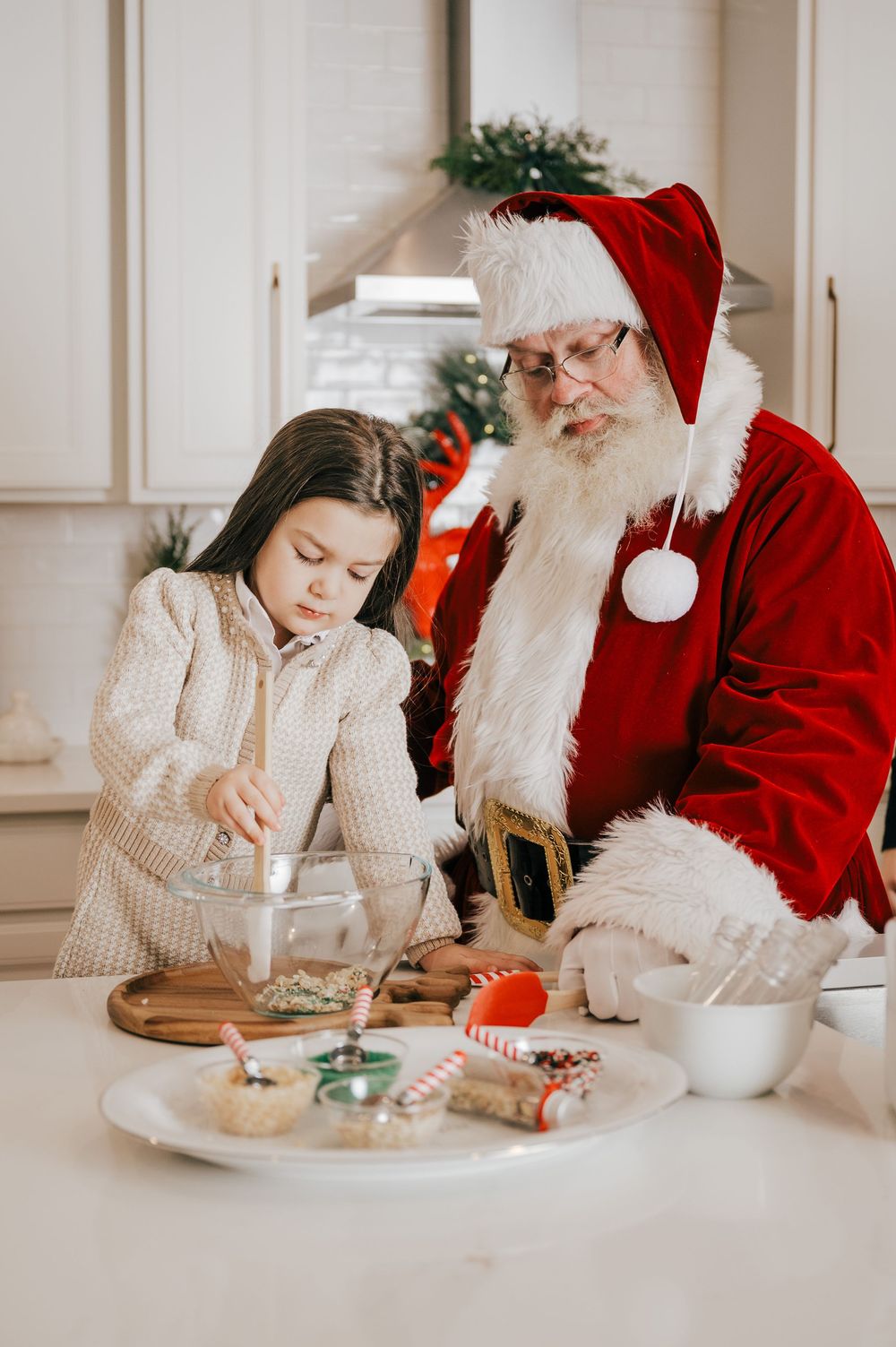 A child and Santa Claus baking Christmas cookies together in a festive kitchen.