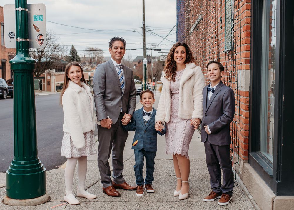 Family of five posing together on a city sidewalk, dressed in formal attire for a special occasion.