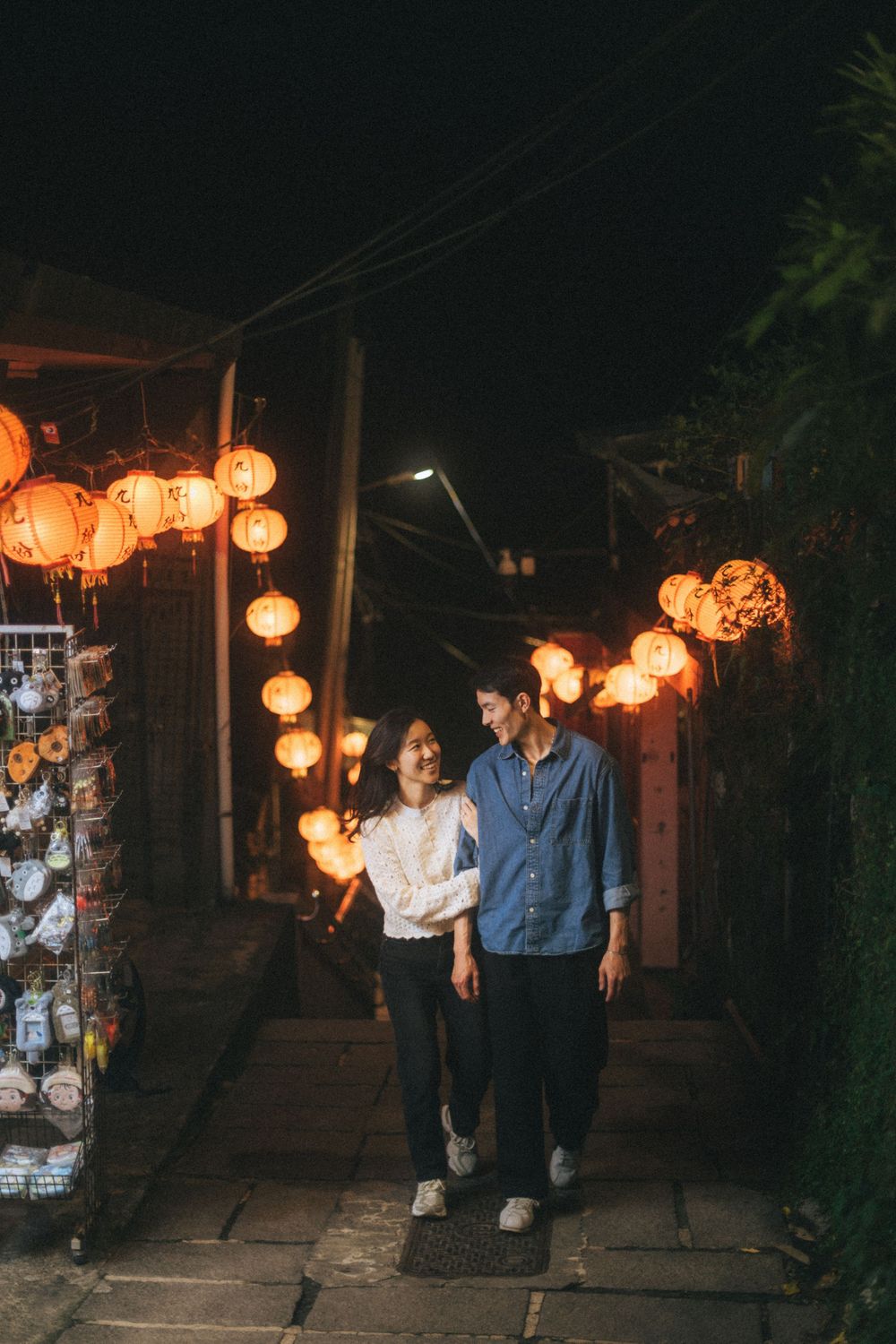 Couple walking under glowing red lanterns at night in a charming Asian alleyway with souvenir shops.