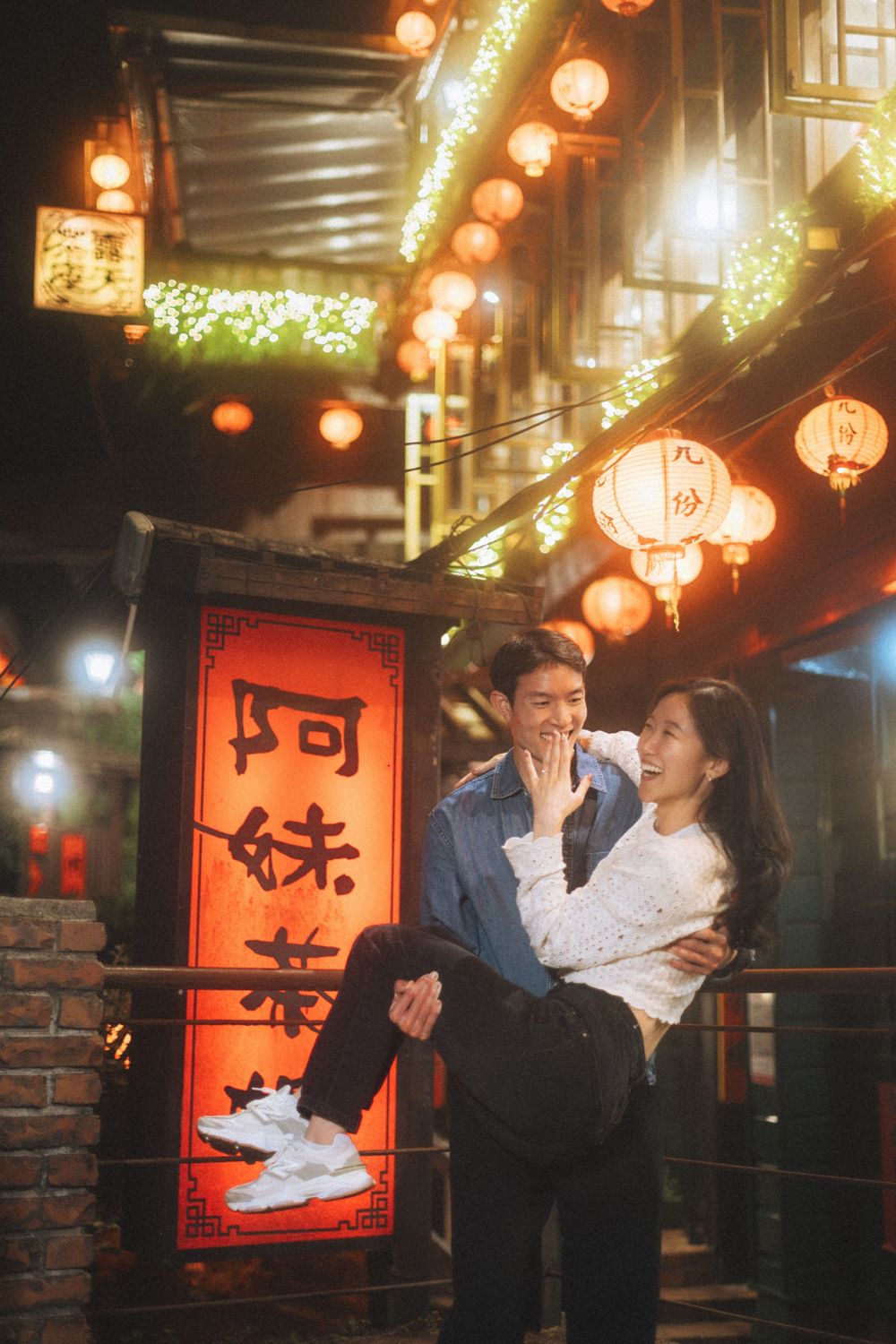 Couple laughing joyfully at night in Jiufen, Taiwan, surrounded by glowing red lanterns and traditional signs.