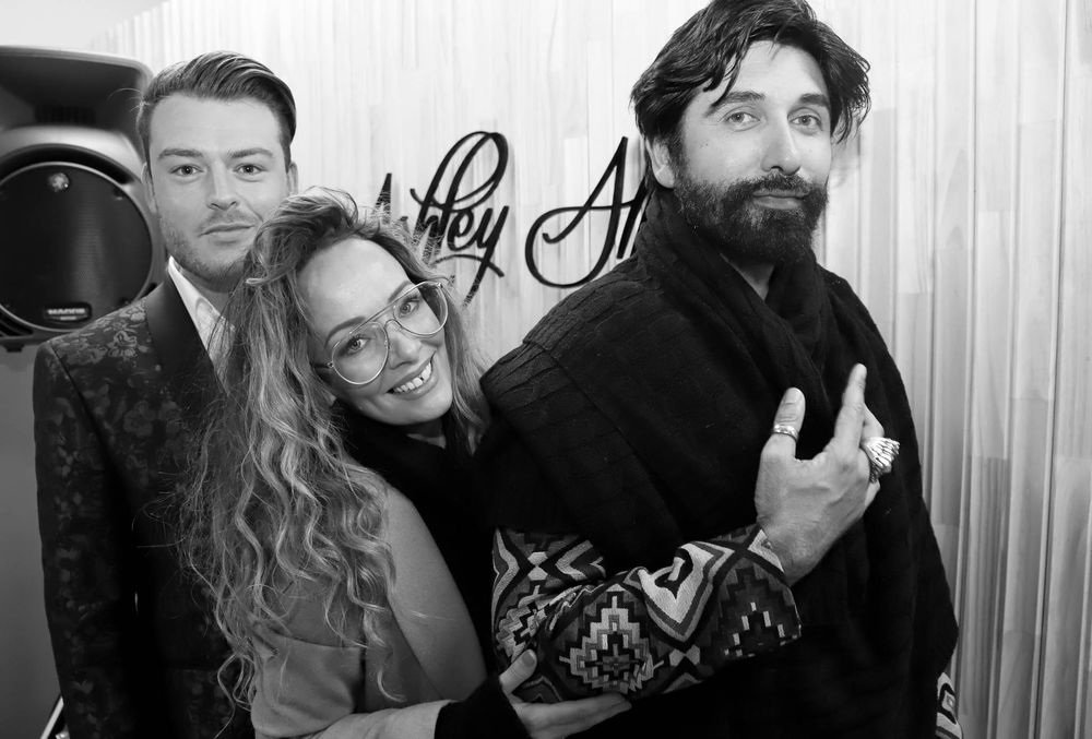 Black and white photo of three smiling people posing together indoors at a social event.