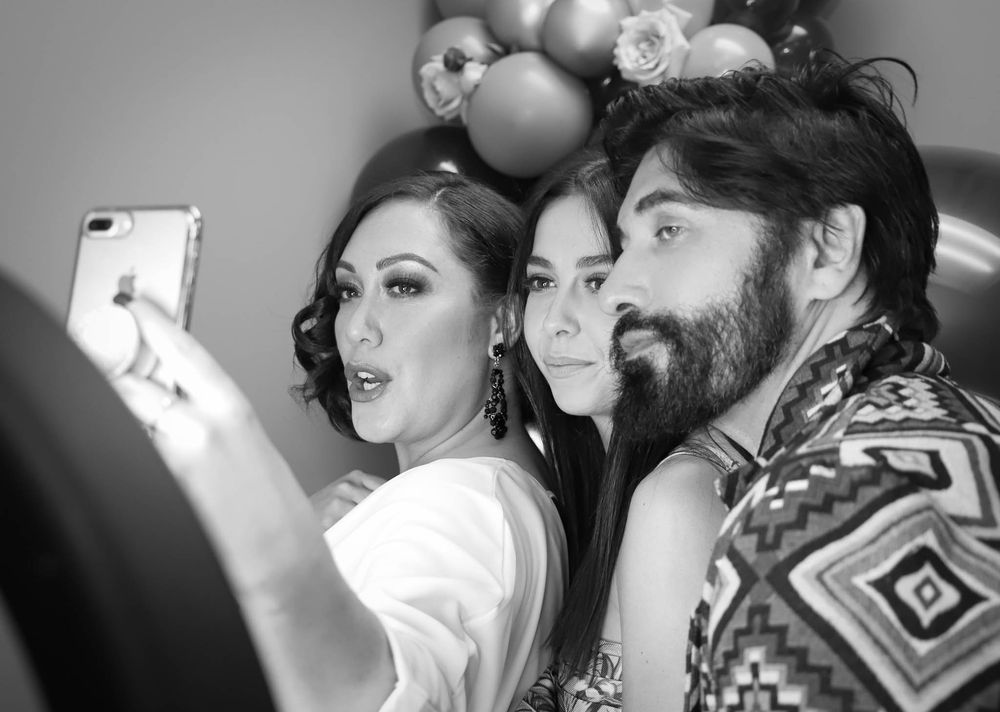 Three people pose for a selfie in black and white photo with balloon decorations in the background.