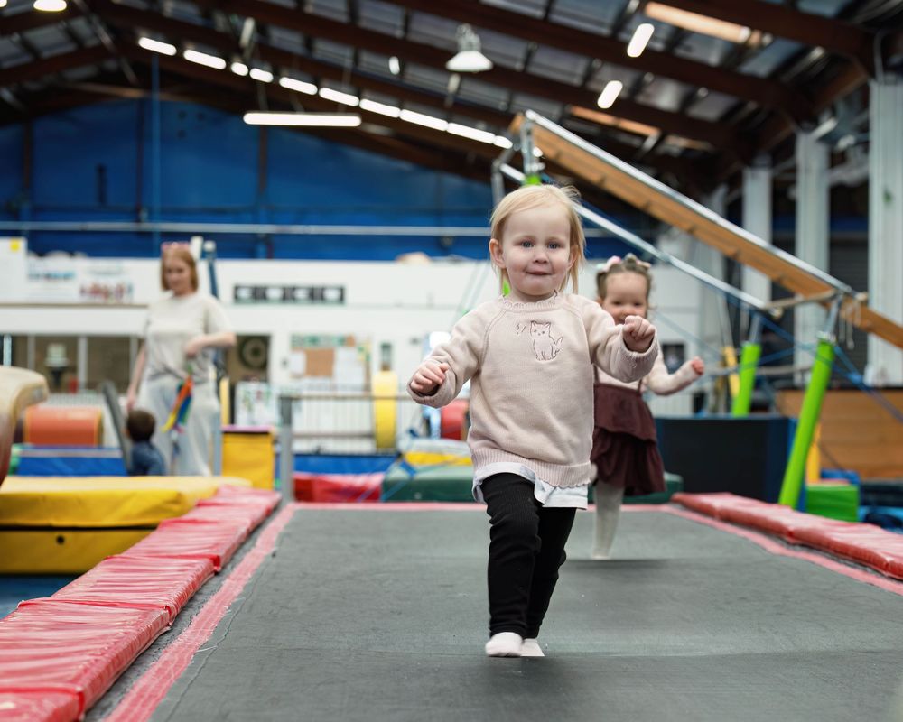 Two toddlers playing on a trampoline in a colorful indoor gymnastics center with foam equipment.