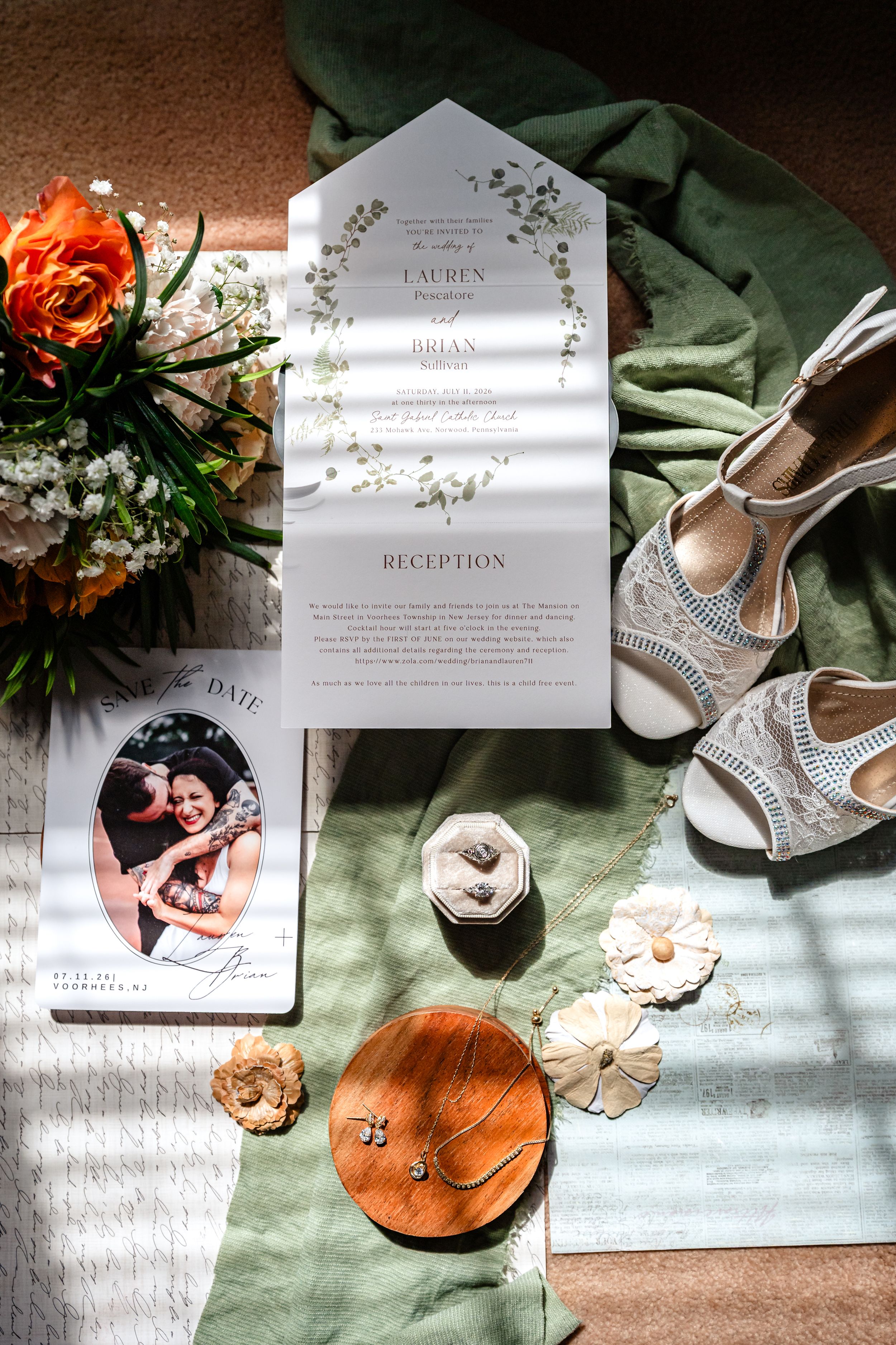 Wedding flat lay with invitation suite, bridal heels, bouquet, and accessories on green linen.