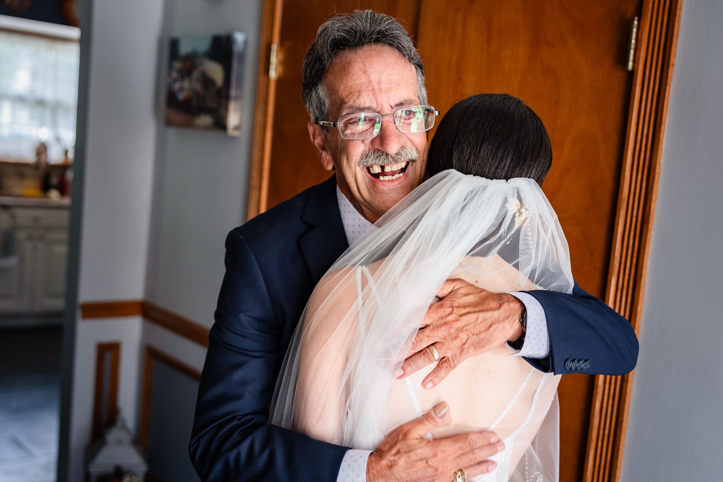Emotional father hugging bride in wedding veil and dress before ceremony begins.