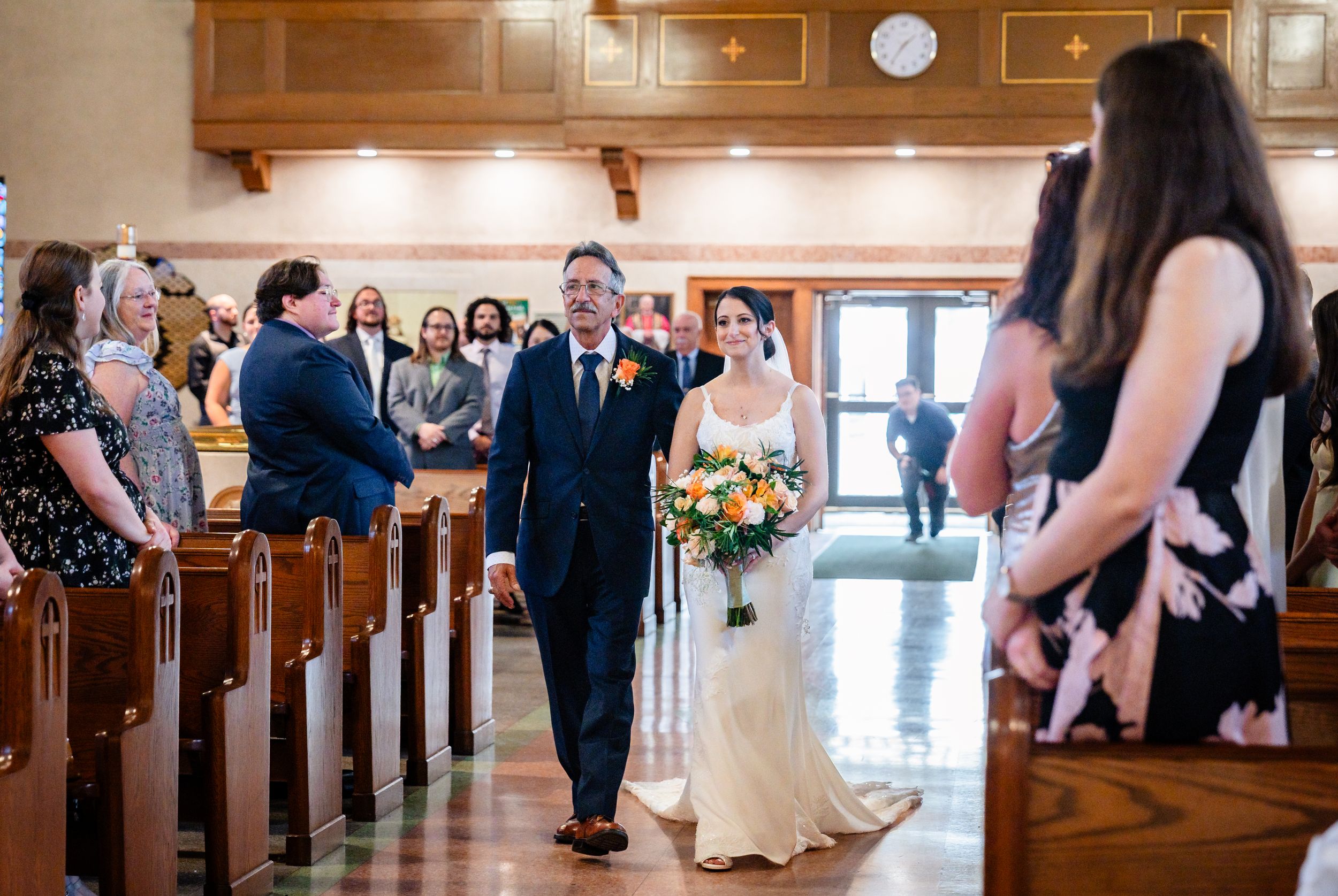 Bride walks down church aisle with escort holding bouquet of flowers during wedding ceremony.
