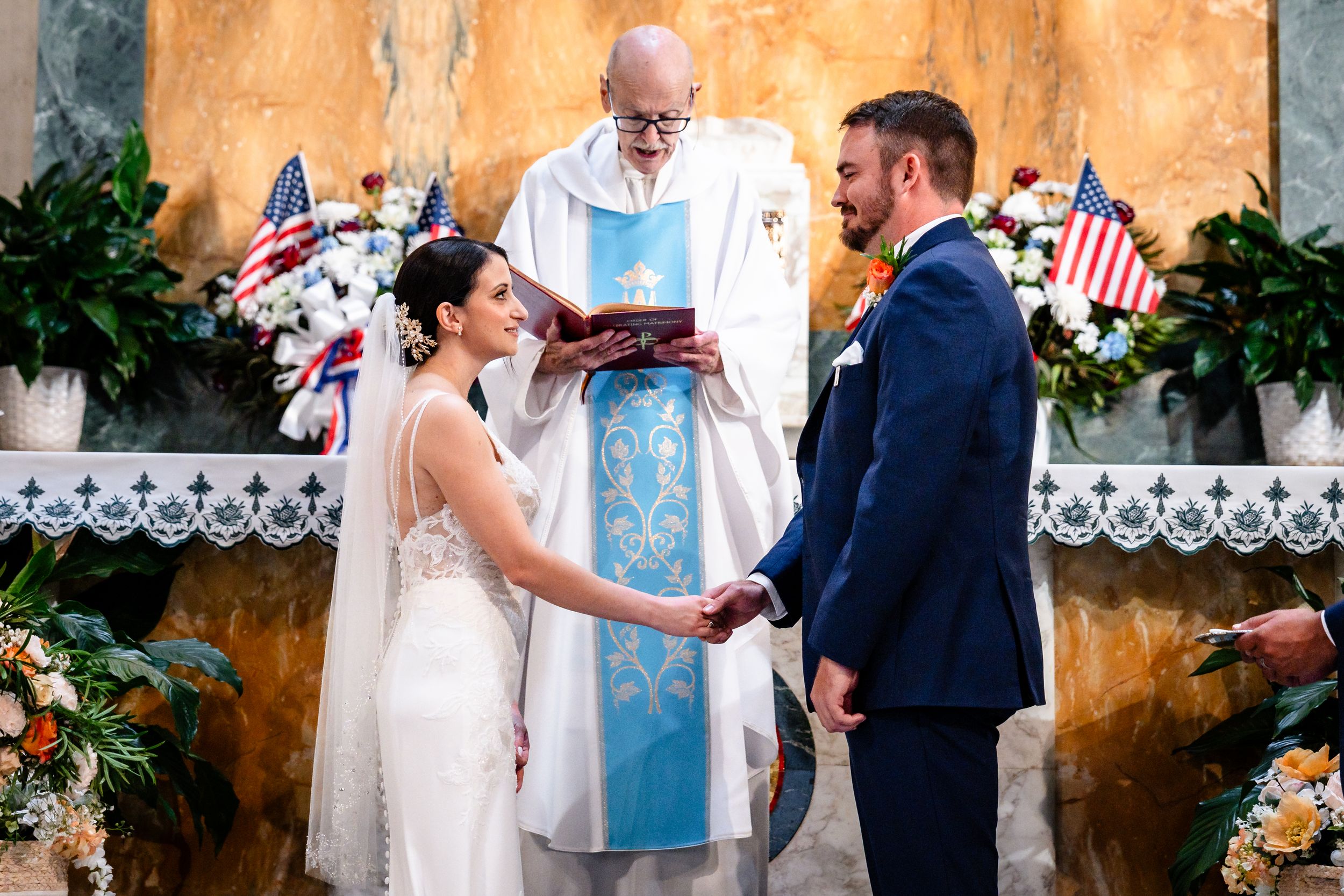 Bride and groom exchanging vows holding hands before officiant at church wedding ceremony altar.