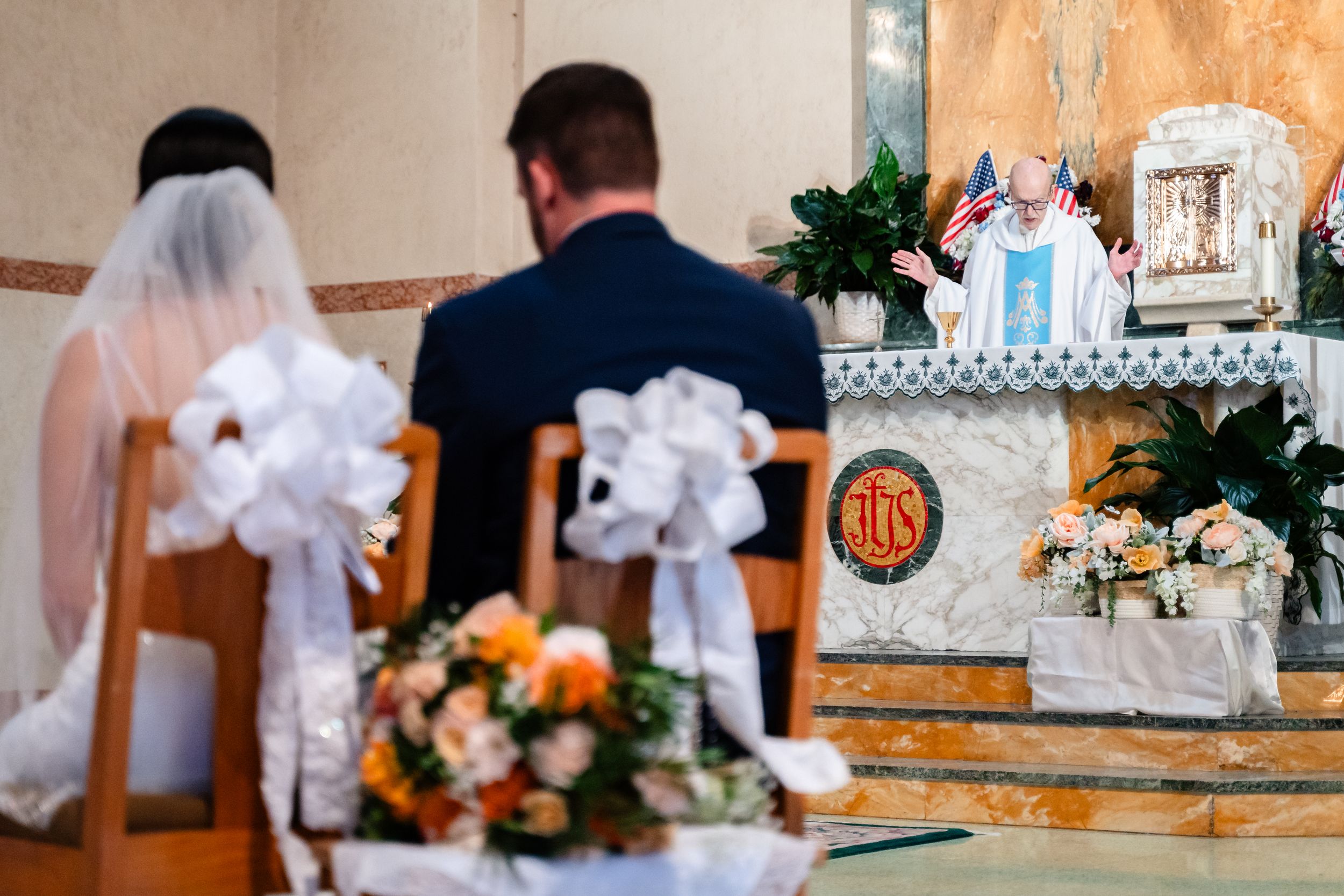 Couple kneeling at church altar during wedding ceremony with priest officiating.