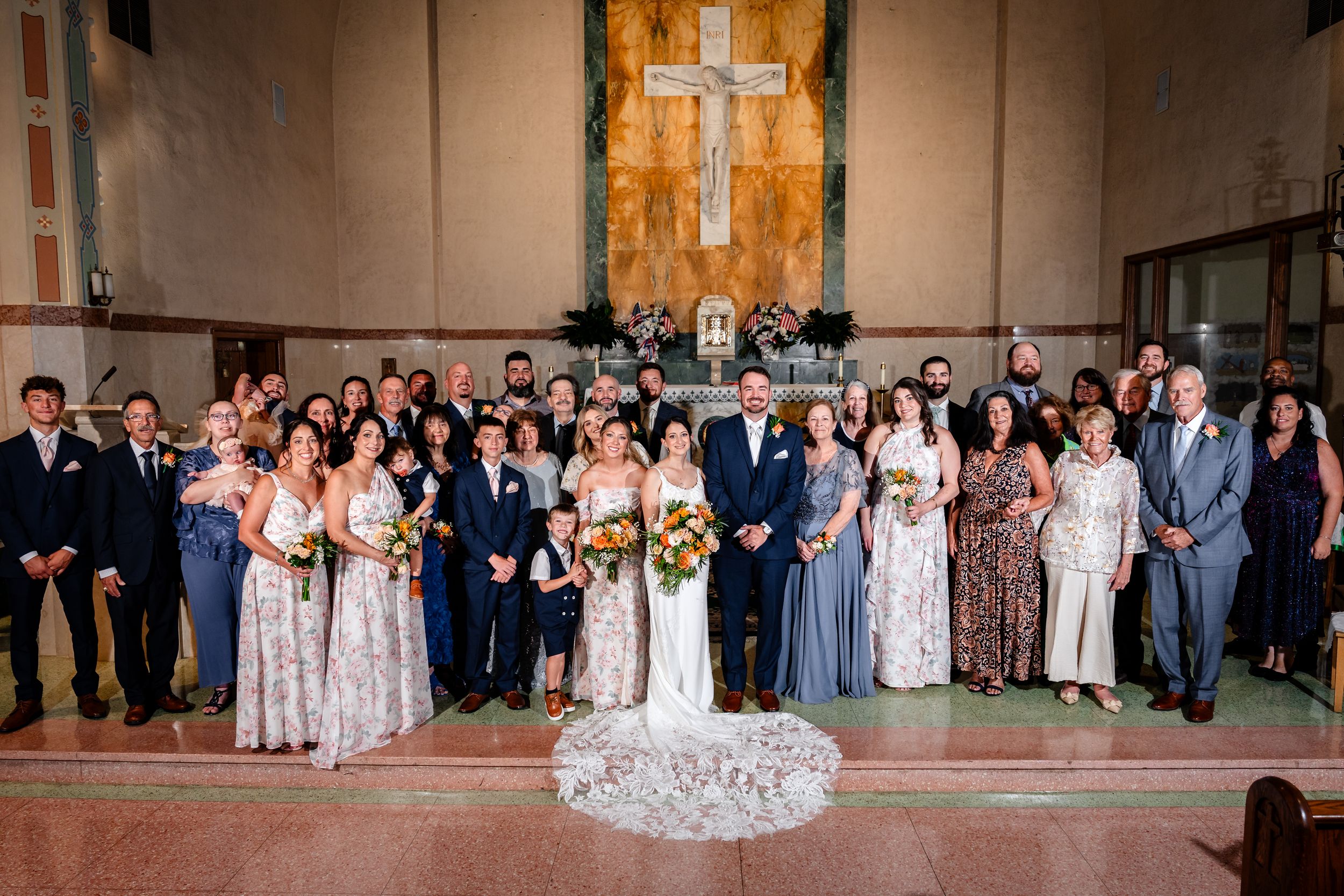 Large wedding party group photo inside church with cross backdrop.