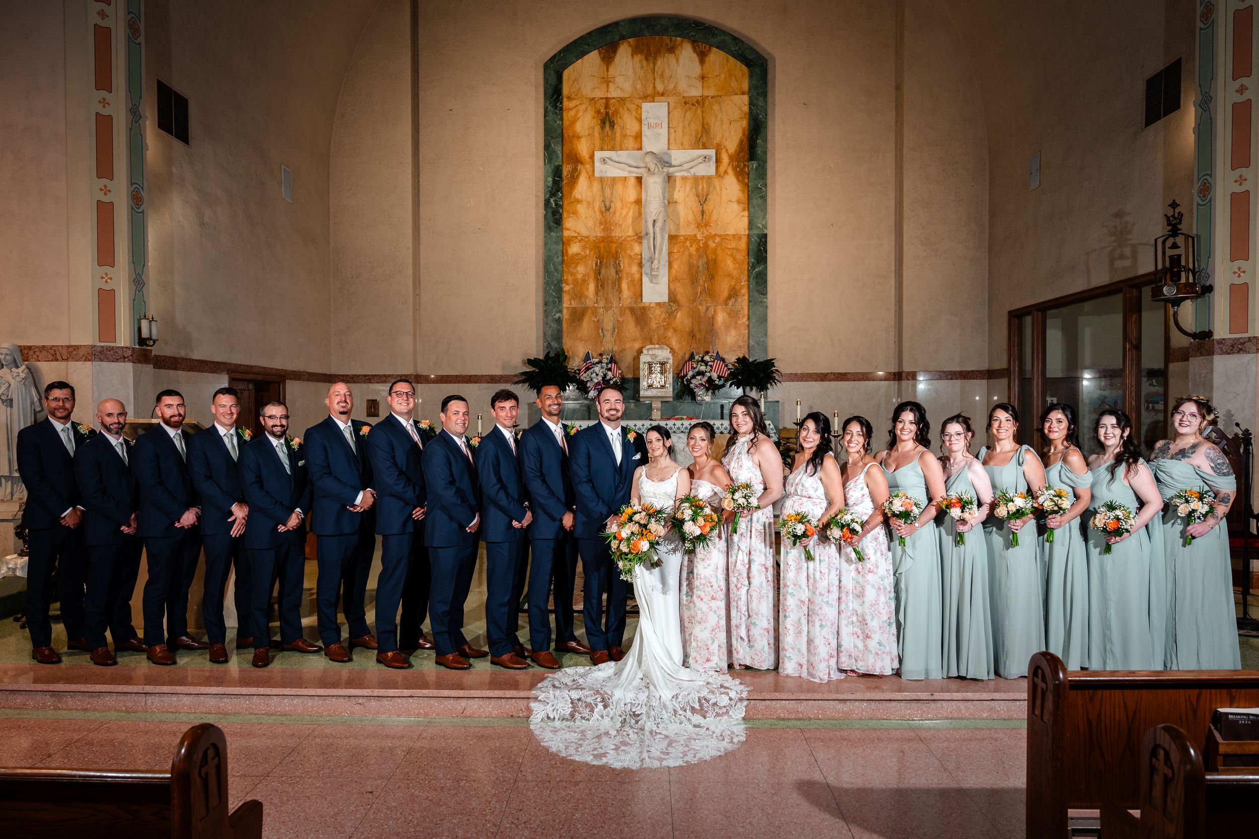 Wedding party lineup in church with bridesmaids in sage green and groomsmen in navy.