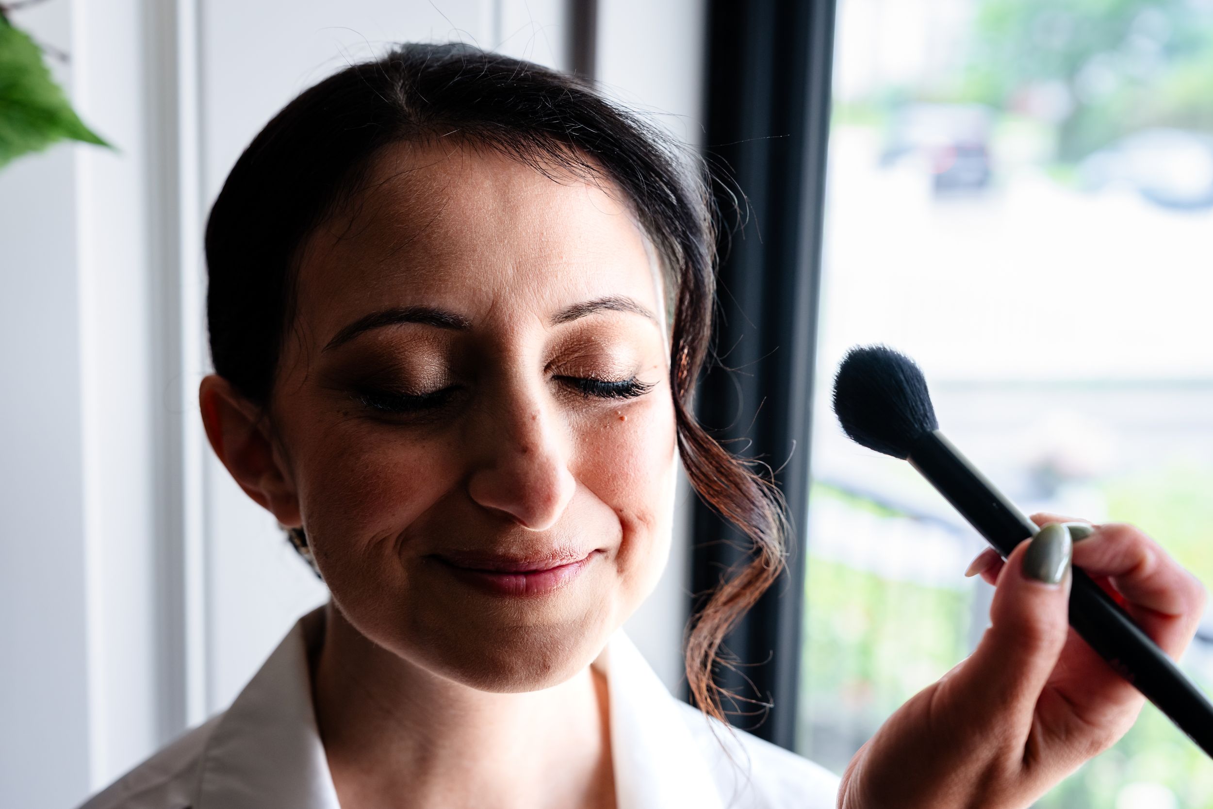 Bride getting professional makeup applied with powder brush during wedding day preparations.