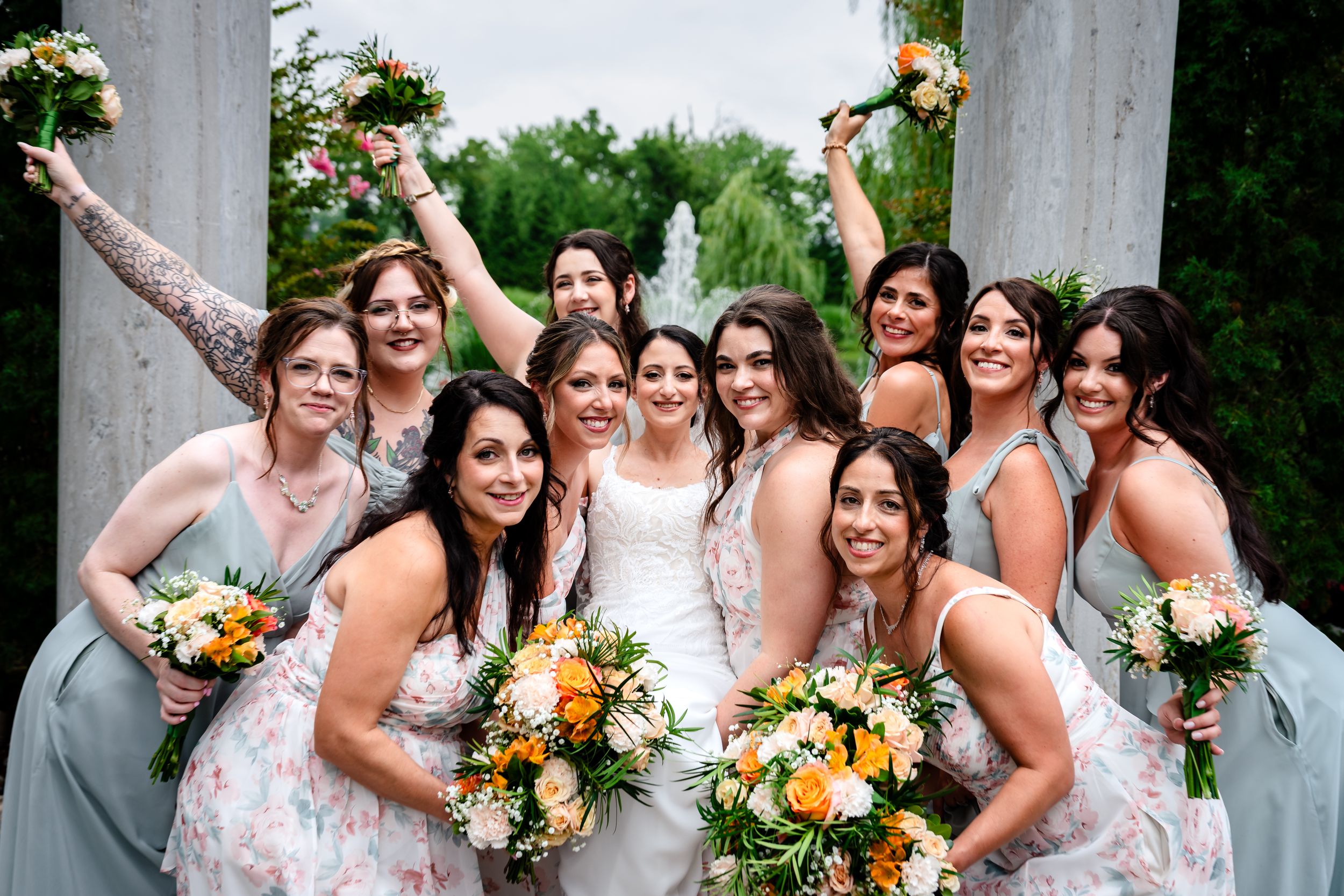Bridesmaids in sage green dresses celebrating with bride holding orange bouquets.