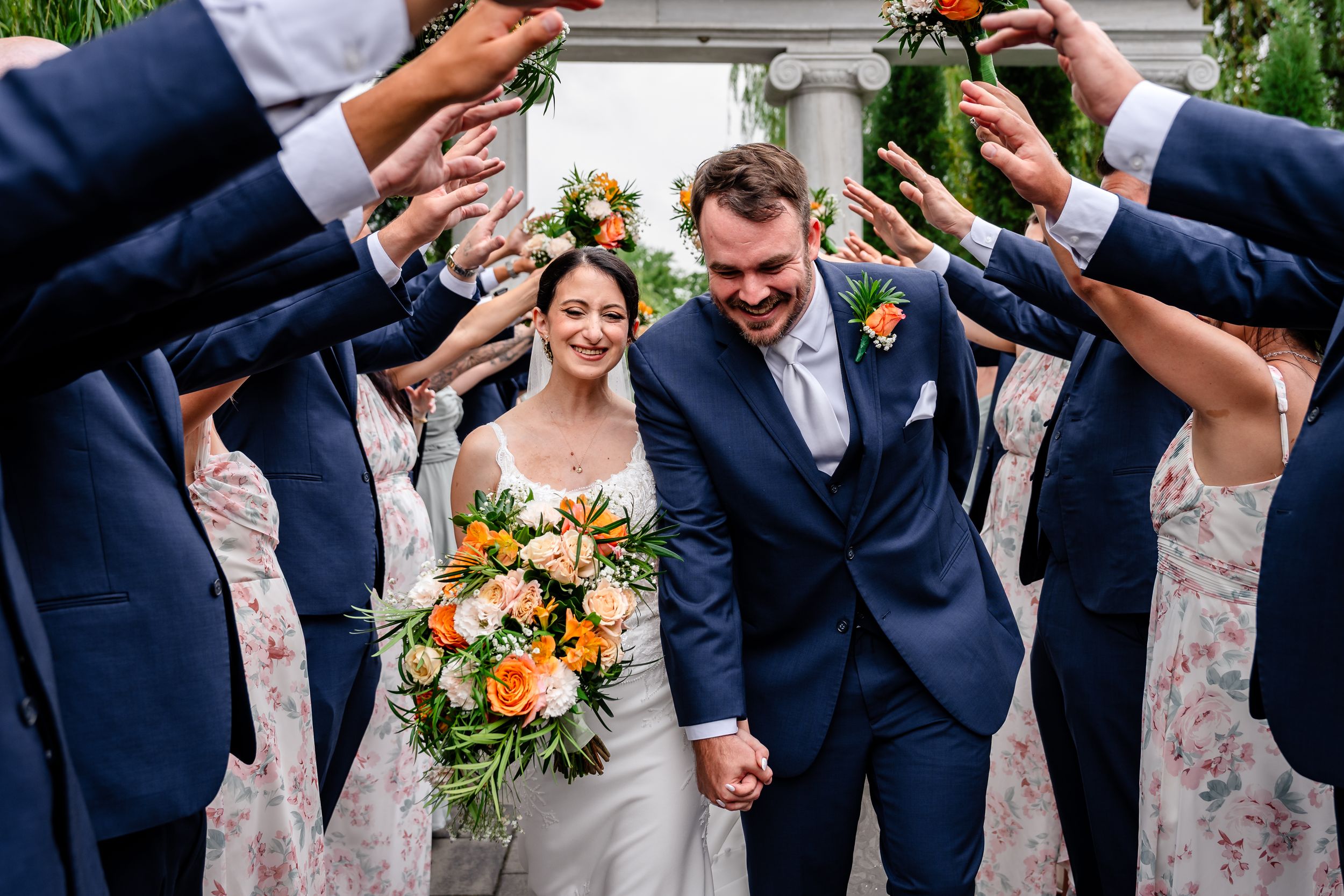 Bride and groom walking through arch of raised hands with wedding party.