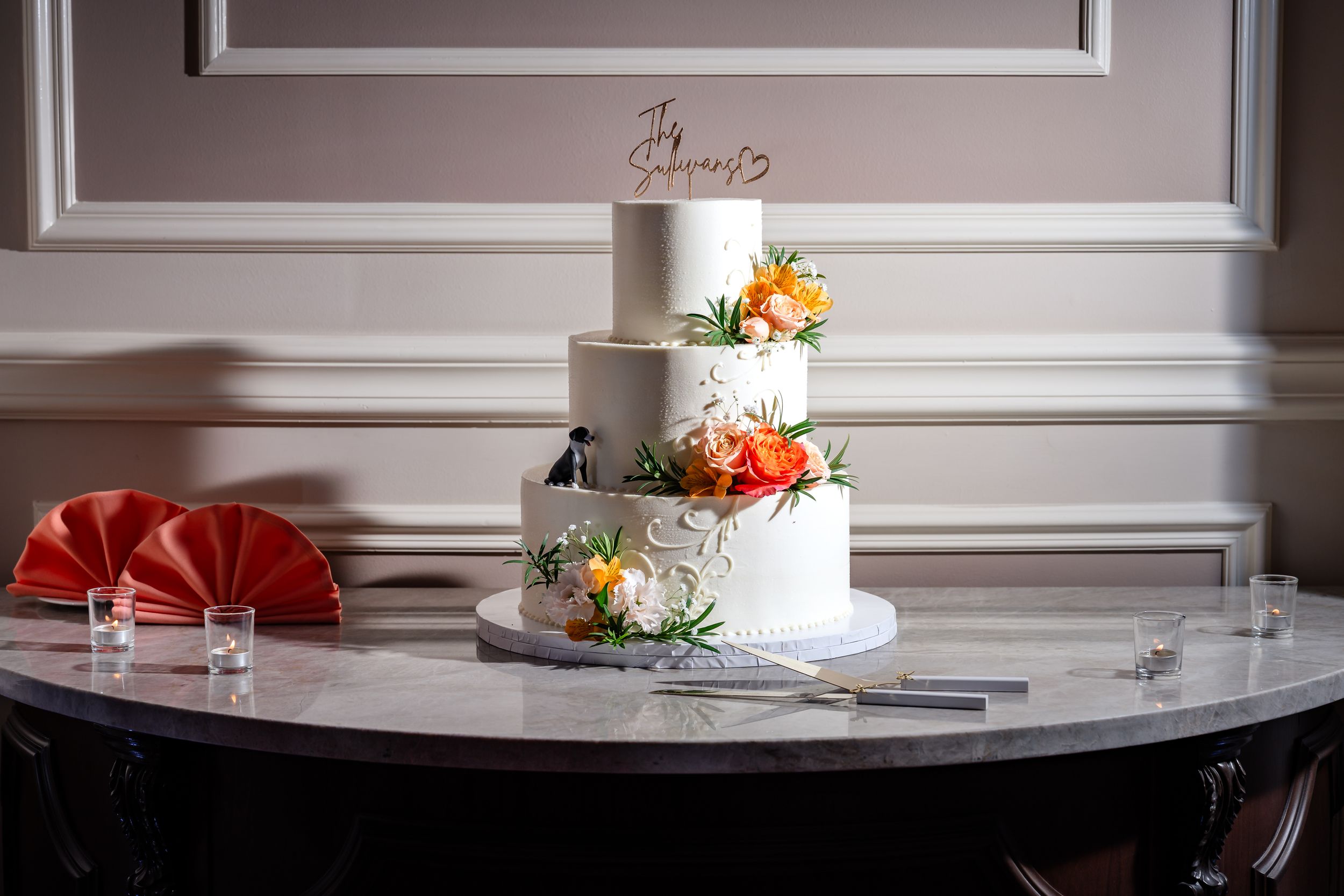 Elegant three-tier white wedding cake with orange and yellow floral decorations on a marble table.