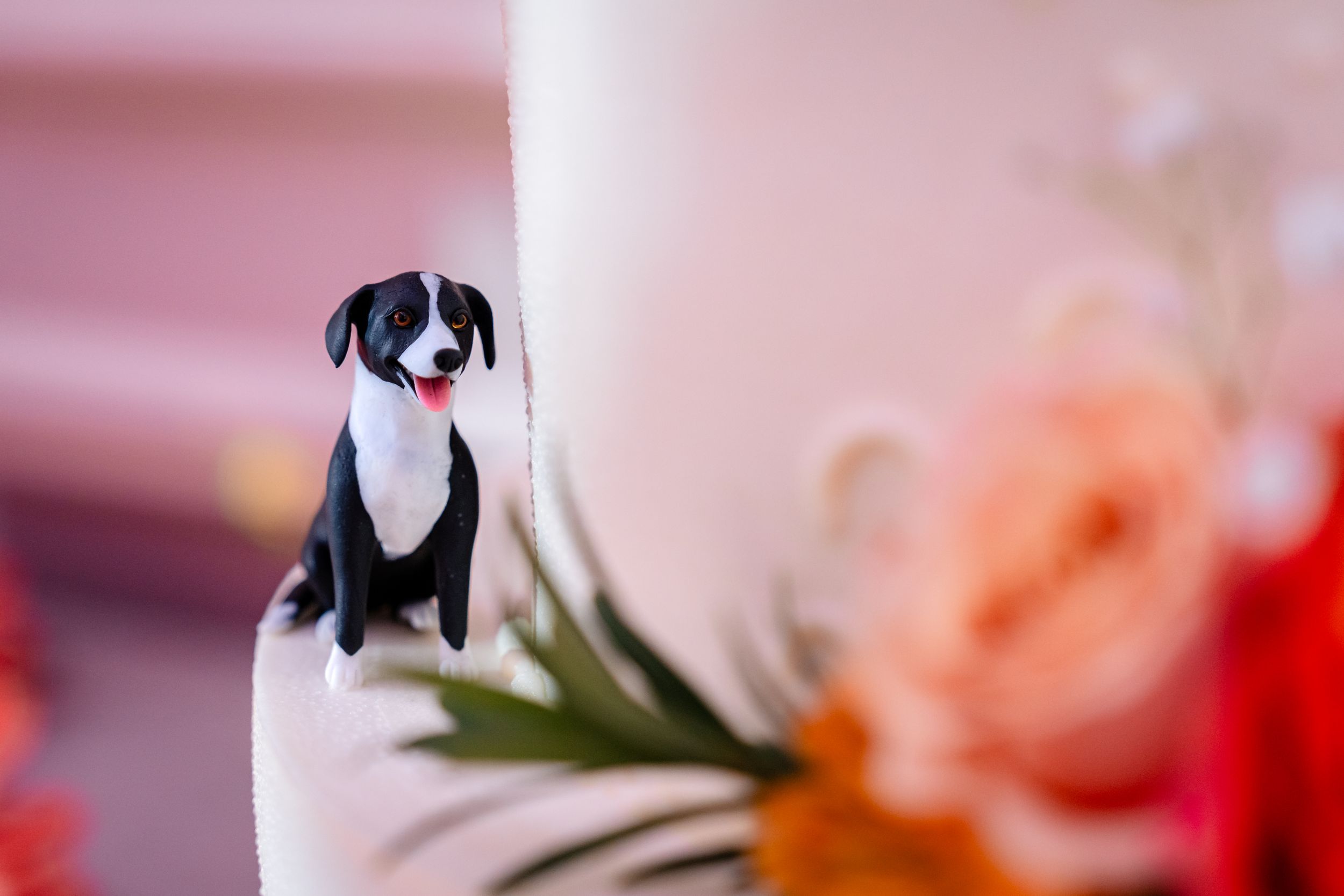 Cute black and white dog figurine cake topper on a white wedding cake with floral decorations.