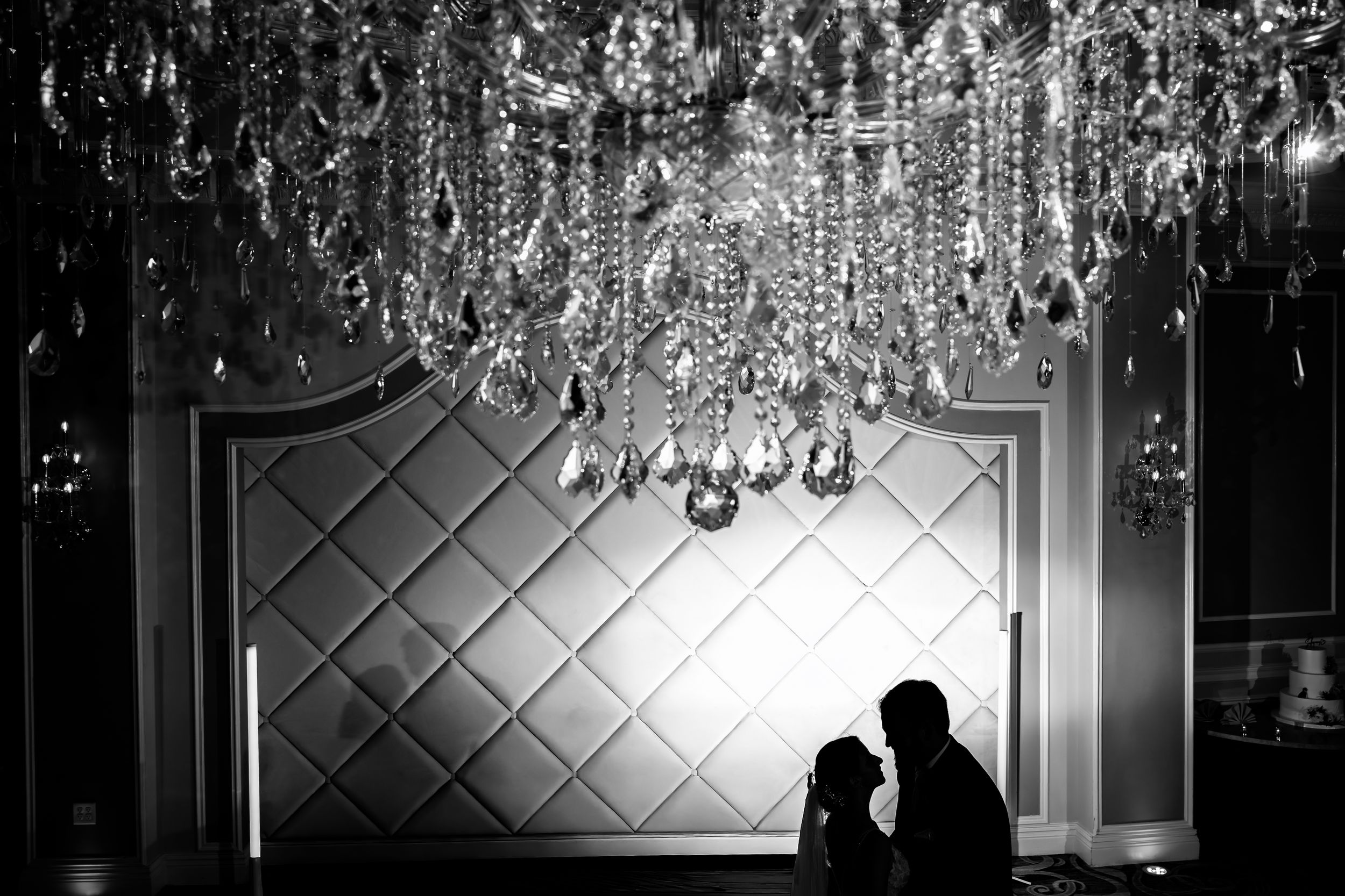 Black and white silhouette of a couple sharing an intimate moment under a crystal chandelier.