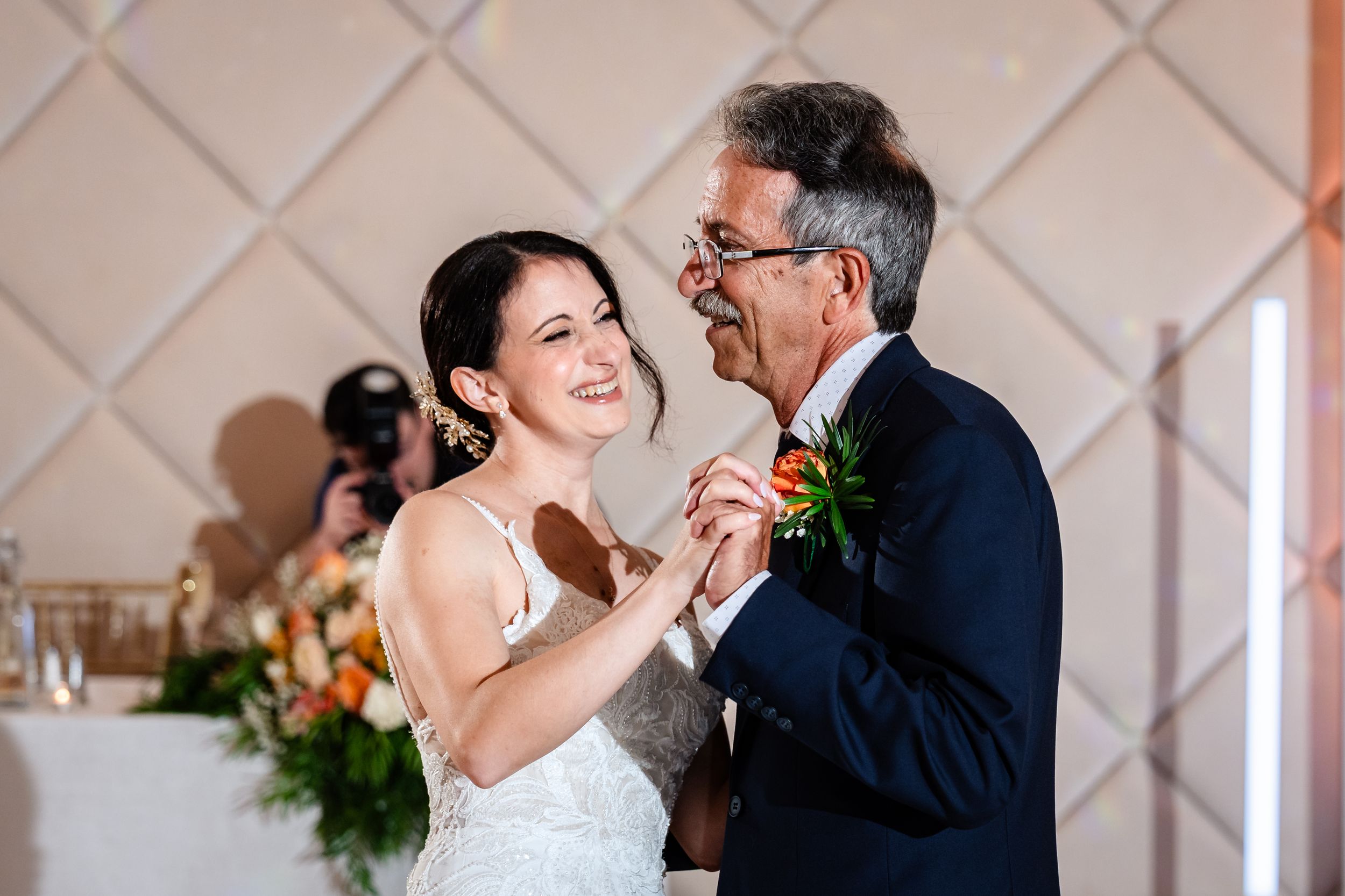 Bride and father share a joyful first dance at wedding reception, smiling warmly in elegant venue.