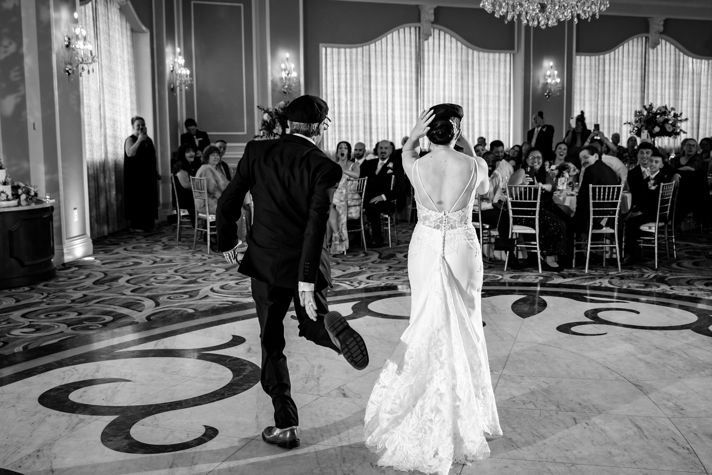 Black and white photo of bride and groom making grand entrance at elegant wedding reception ballroom.