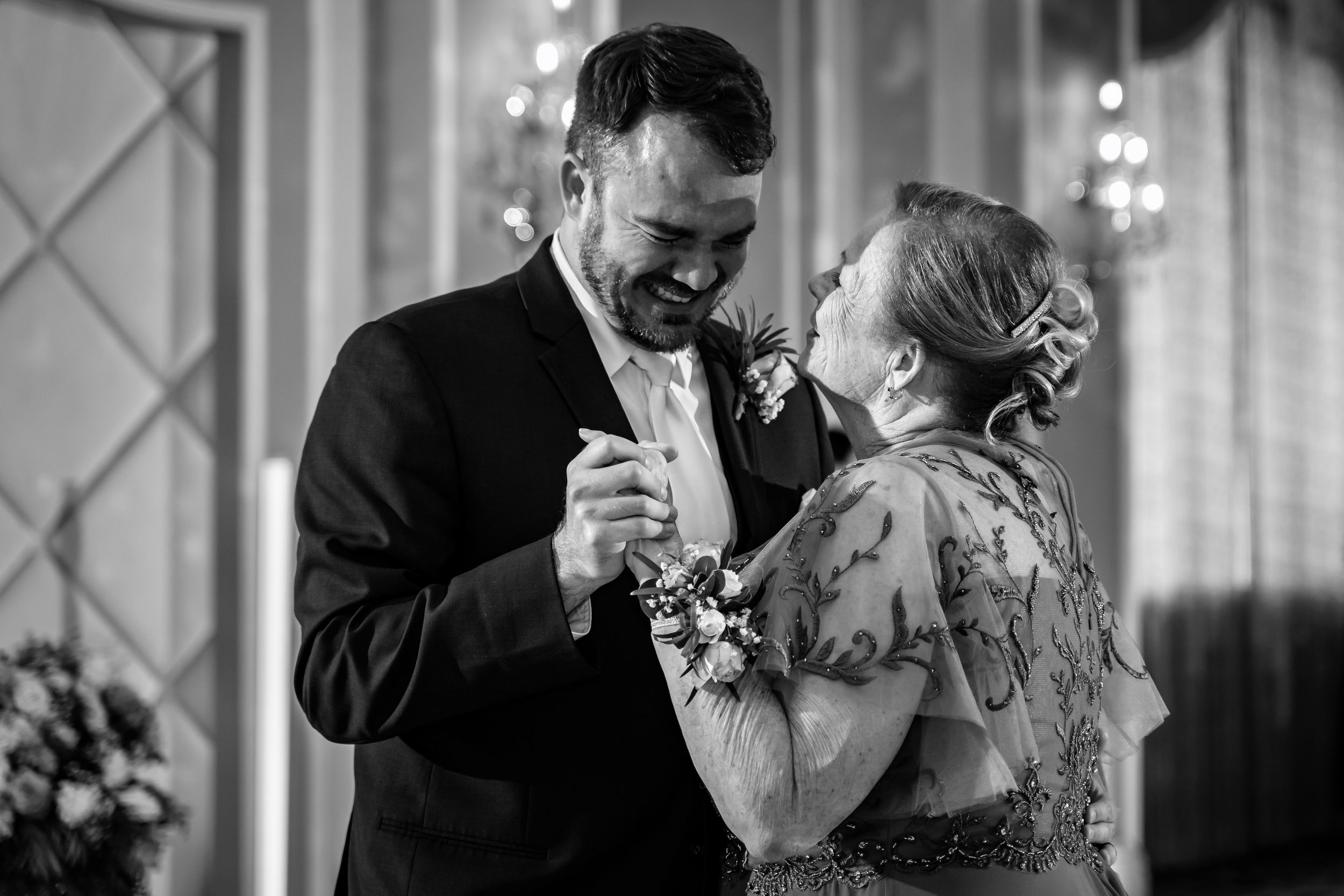 Groom shares emotional mother-son dance at wedding reception in black and white photography.