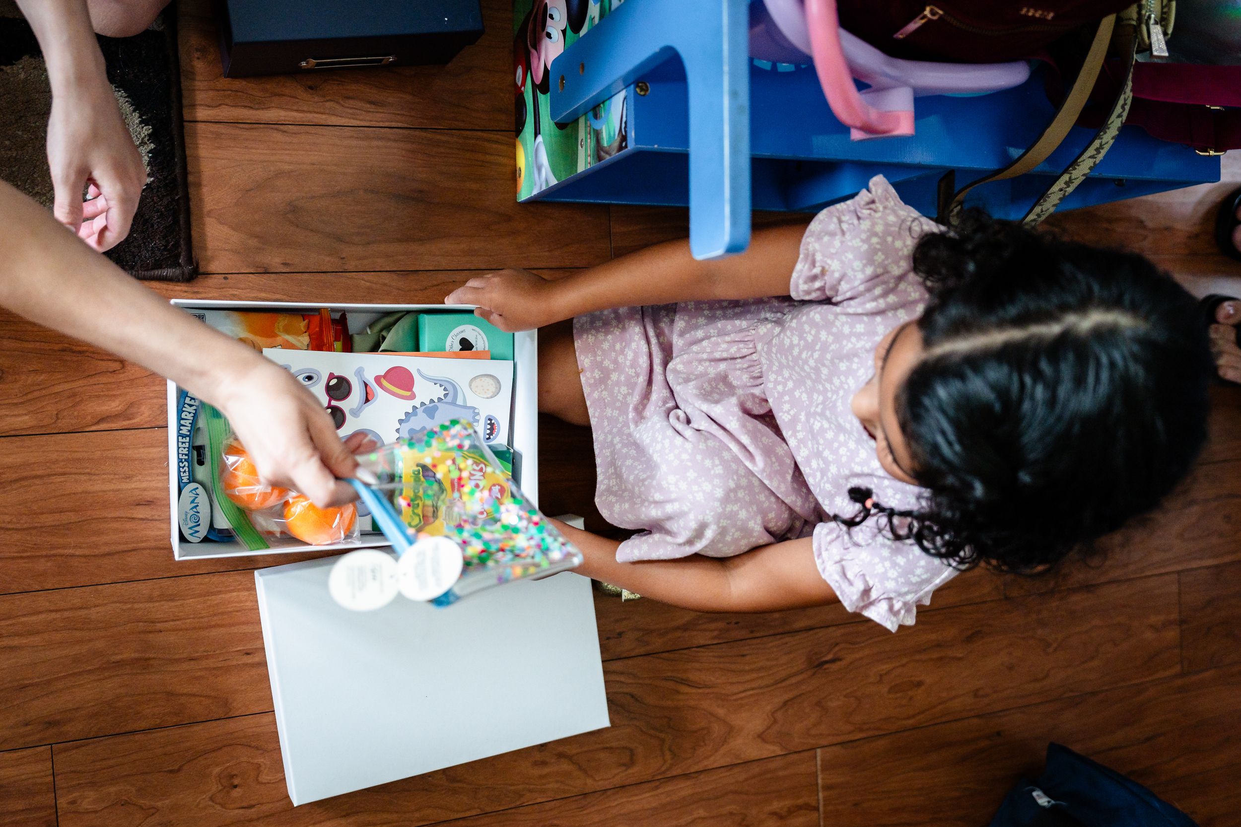 Young girl playing with colorful toys and books on hardwood floor from overhead view.