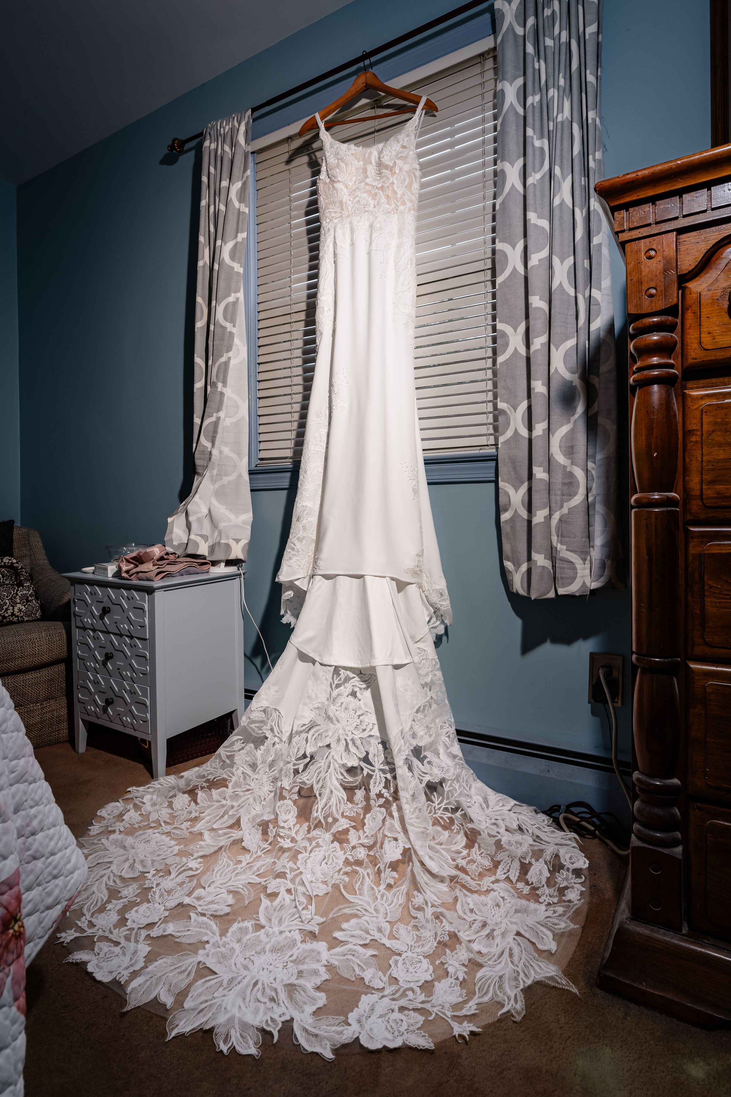 Elegant white lace wedding gown with long train hanging in bedroom before the ceremony.