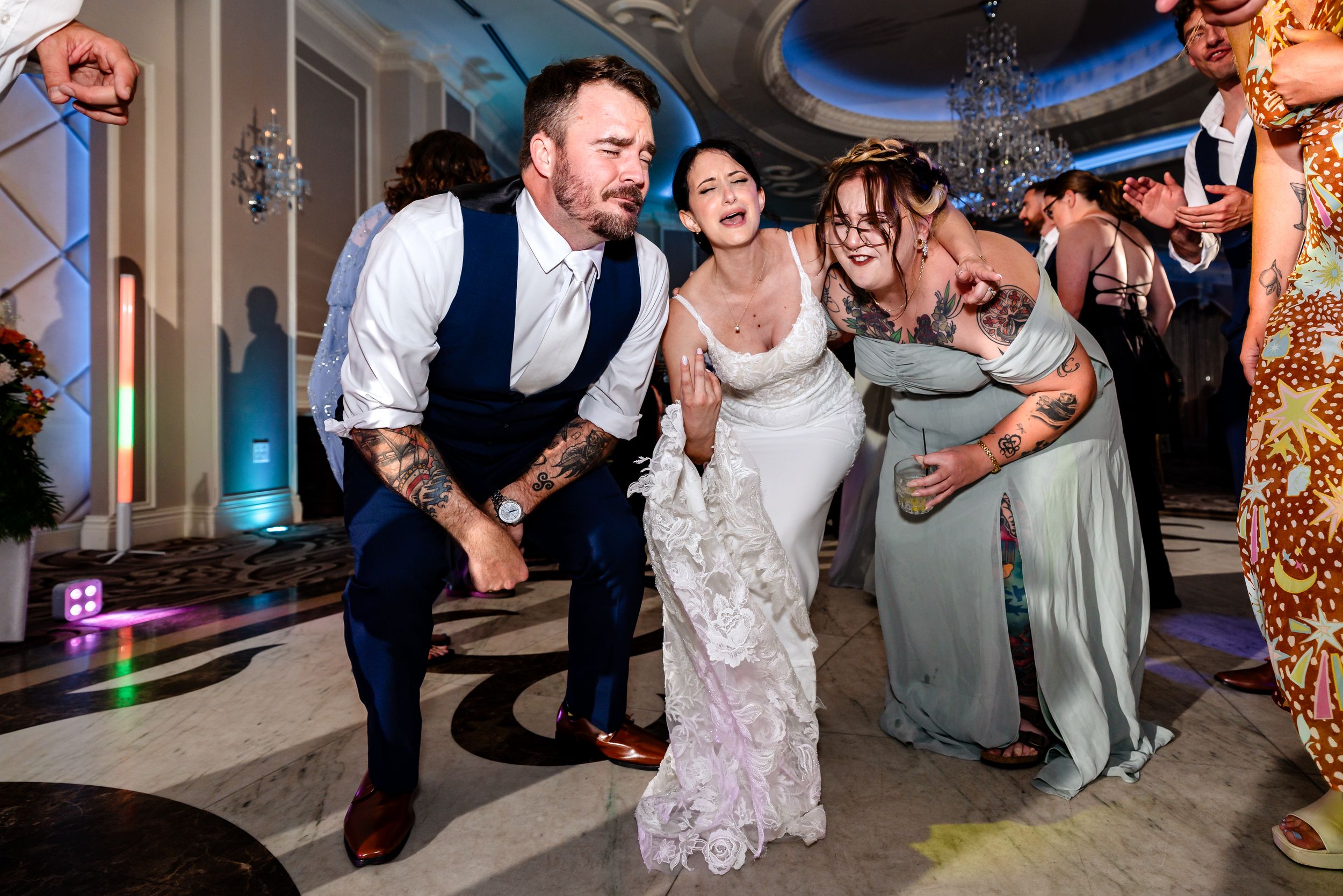 Bride laughing with groom and bridesmaid dancing joyfully at elegant wedding reception.