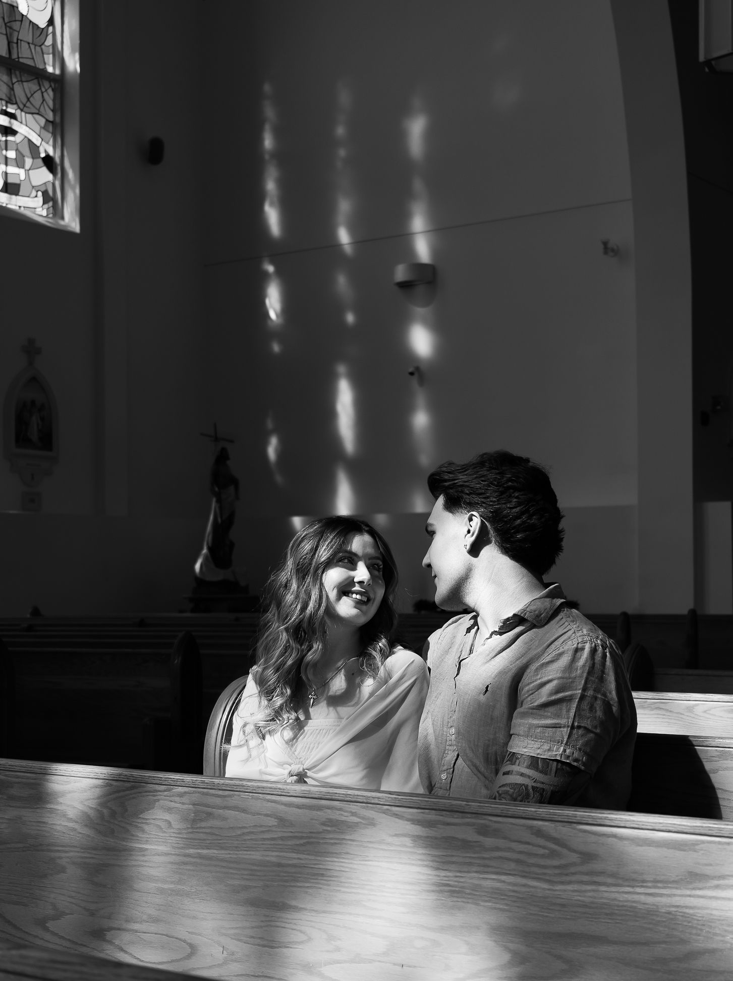 Black and white image of a couple sitting in a church pew, smiling at eachother