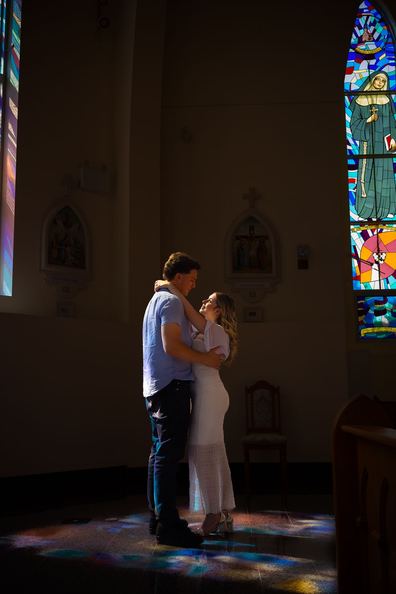 Dark photo of a couple standing in the sunlight from the stained glass windows, dancing/embracing