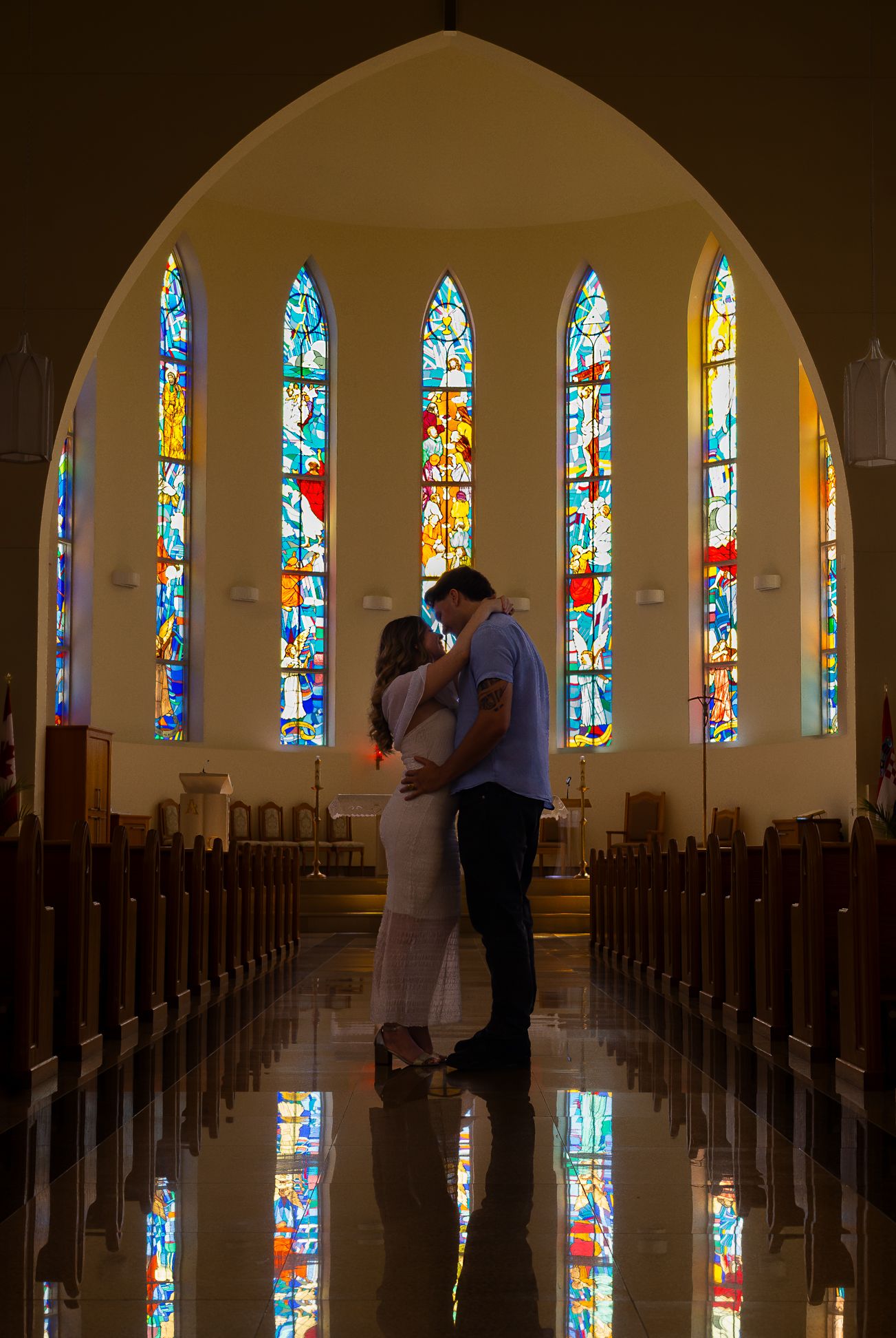 A couple holding each other in the middle of a church, surrounded by stained glass windows