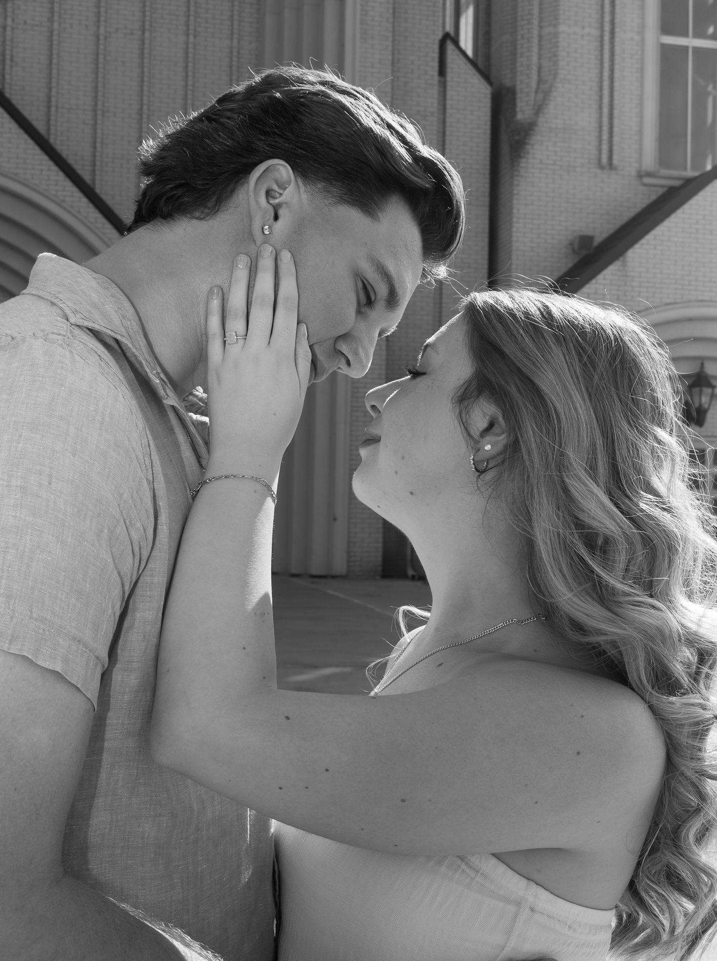 Black and white image of a couple outside a church, embracing, with the womans hand on the mans cheek, staring into each others eyes